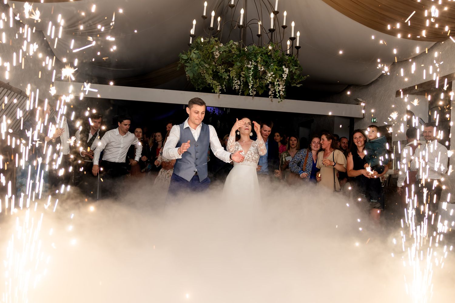Bride and groom share first dance surrounded by sparkling fireworks and fog at elegant wedding reception.