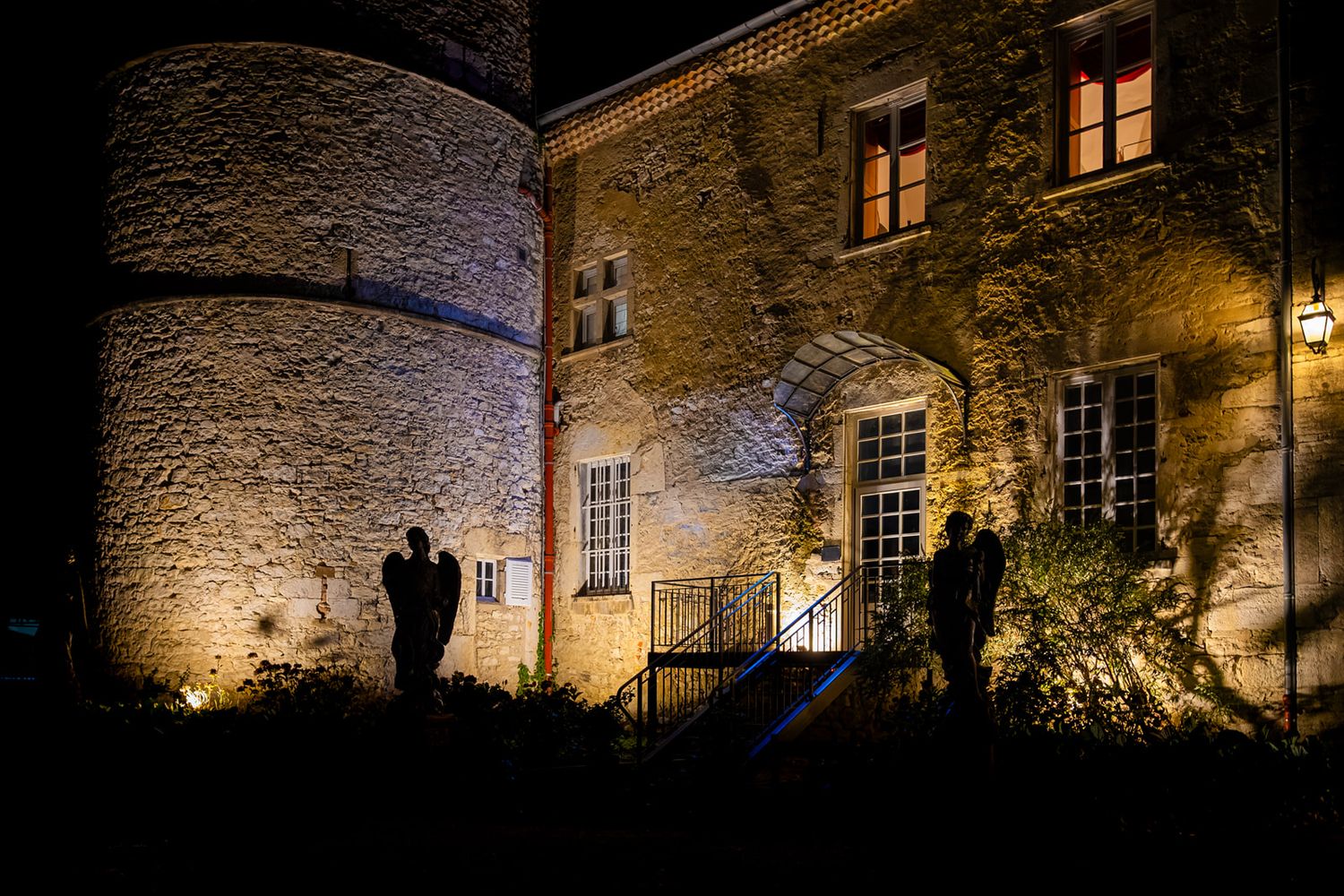 Illuminated stone walls of a historic building at night create a warm, atmospheric glow through windows and archways.