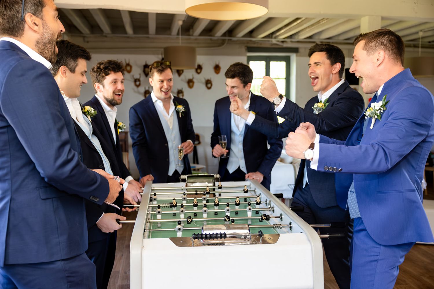Groomsmen in blue suits laughing and playing foosball together at a wedding reception.