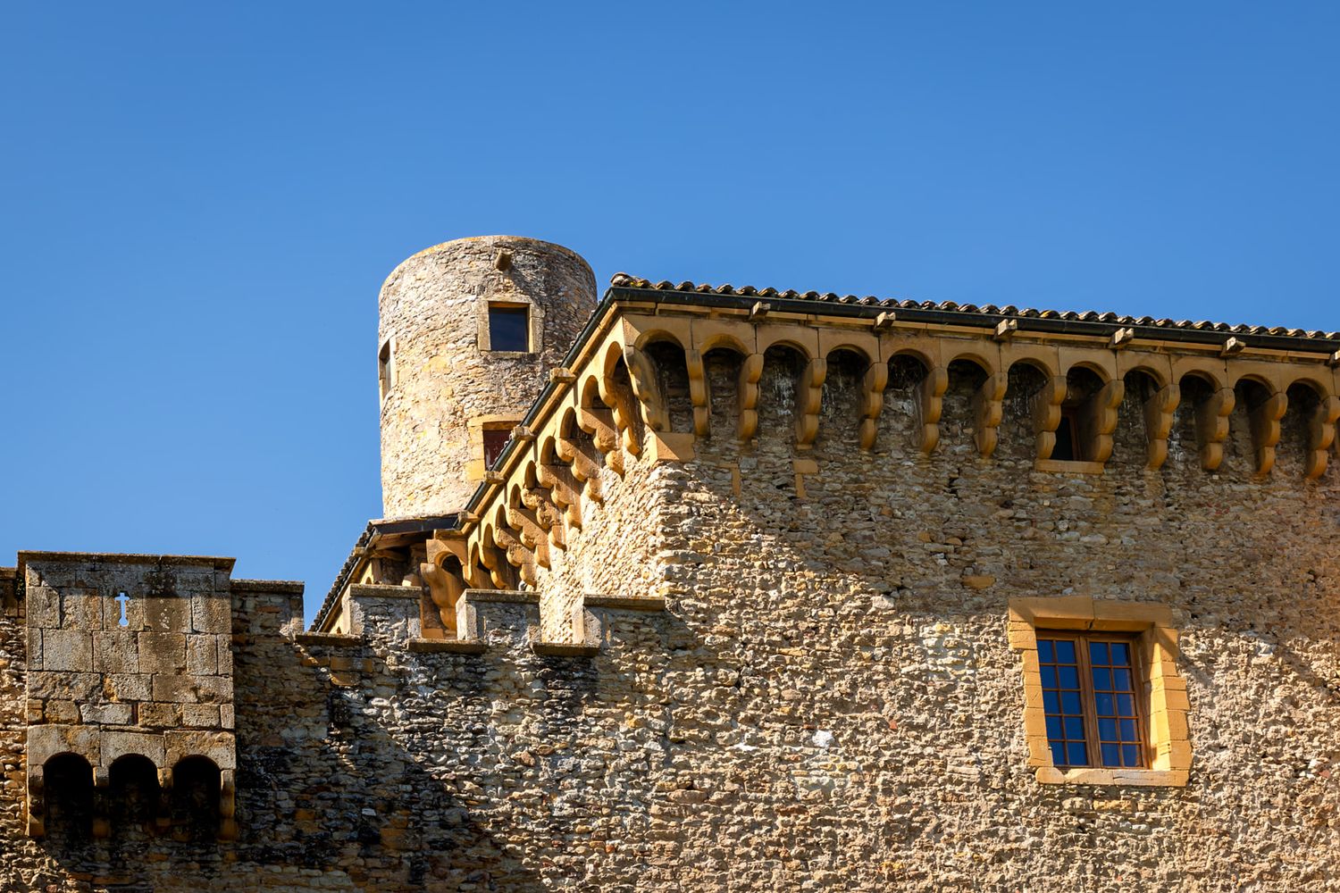 Ancient stone castle wall with arched windows and decorative architectural details against a bright blue sky.