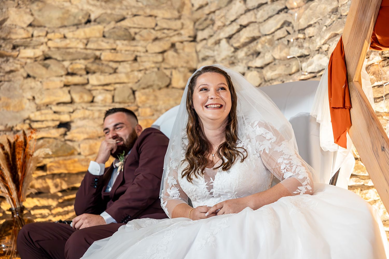 Newlyweds share a joyful moment while sitting on stone steps during their rustic wedding celebration.