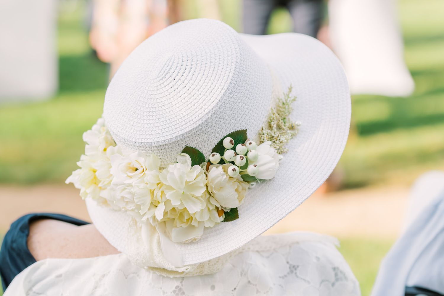 White straw boater hat adorned with fresh white flowers and greenery worn by a woman at an outdoor event.