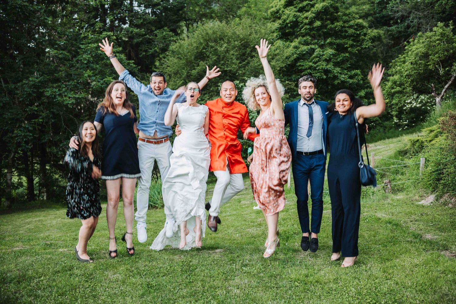 Wedding guests celebrate joyfully on a grassy hillside during an outdoor summer celebration.