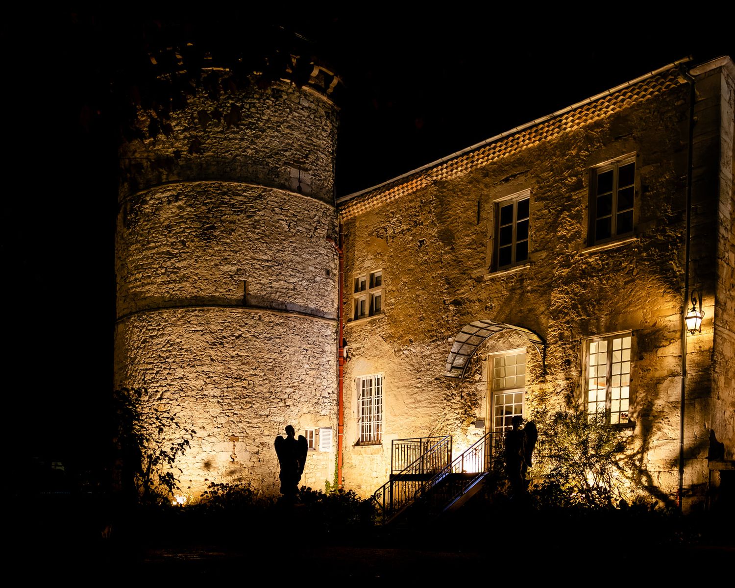 Medieval stone castle illuminated at night with glowing windows and a round tower against dark sky.
