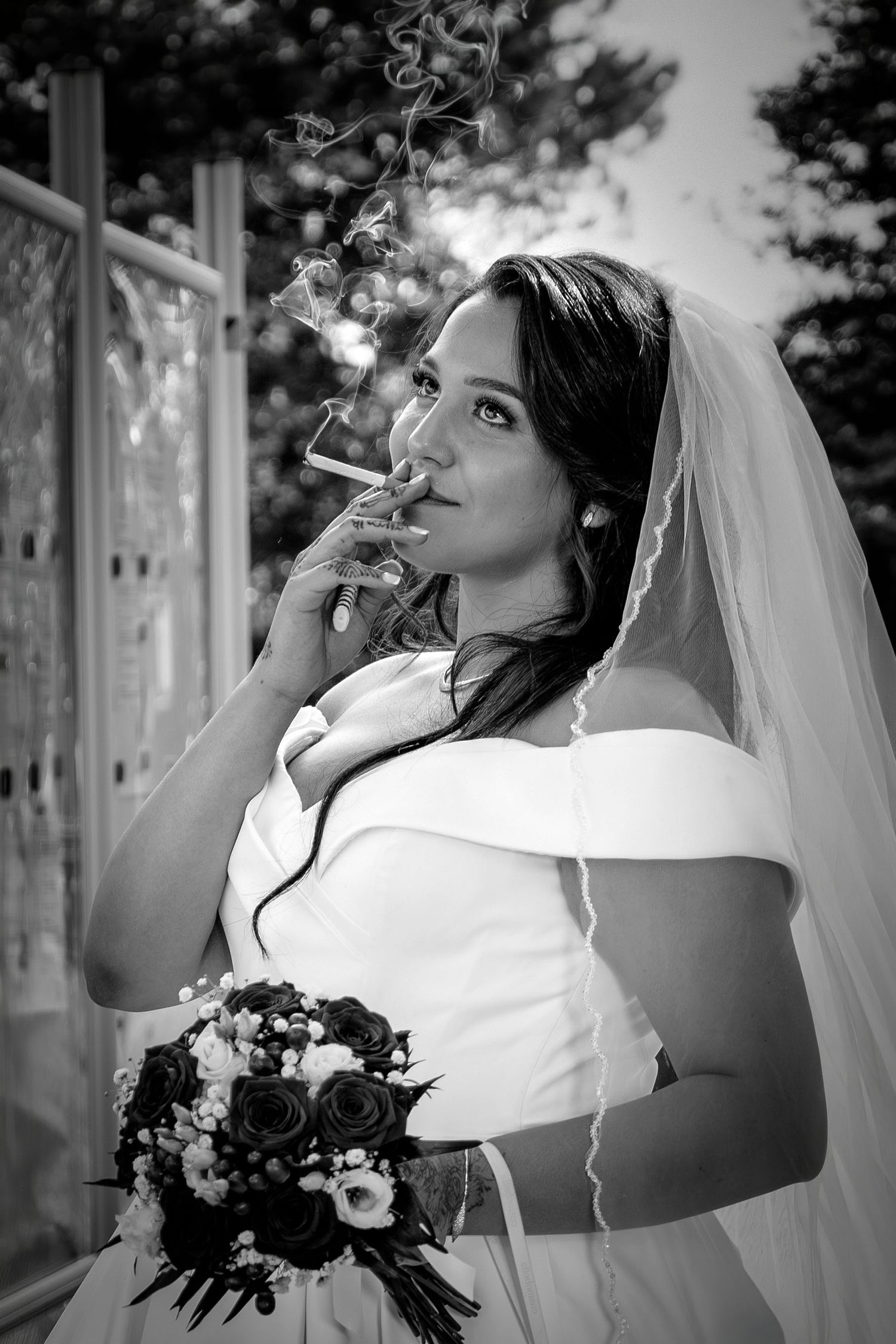 Black and white photo series of a bride in white dress smoking a cigarette while holding a dark floral bouquet.