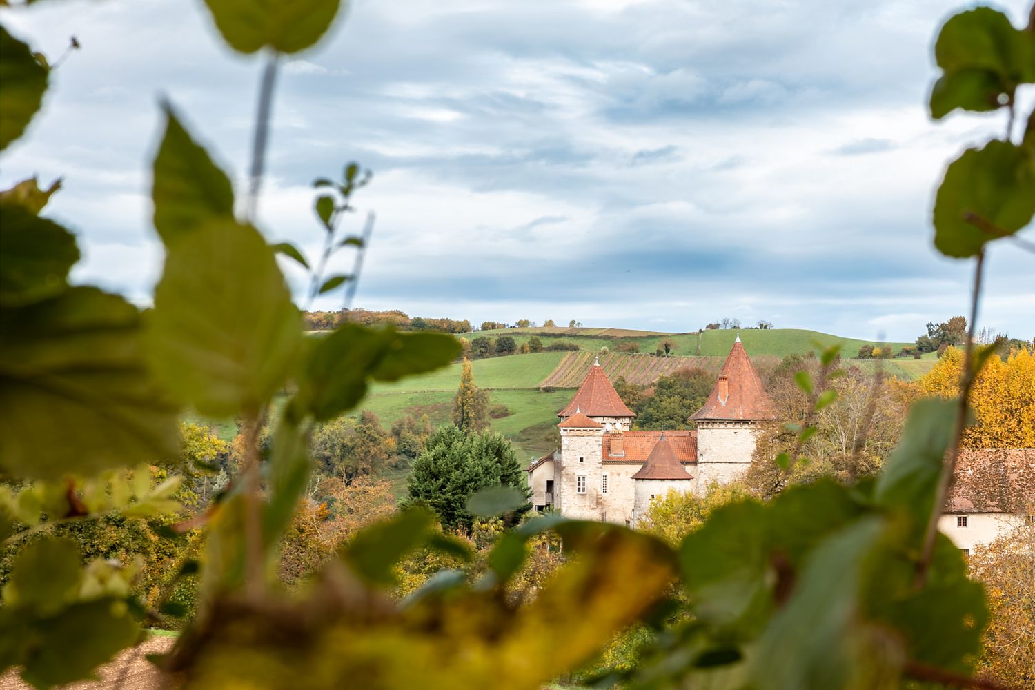 Rolling green hills and countryside landscape with scattered buildings and trees under a cloudy sky.
