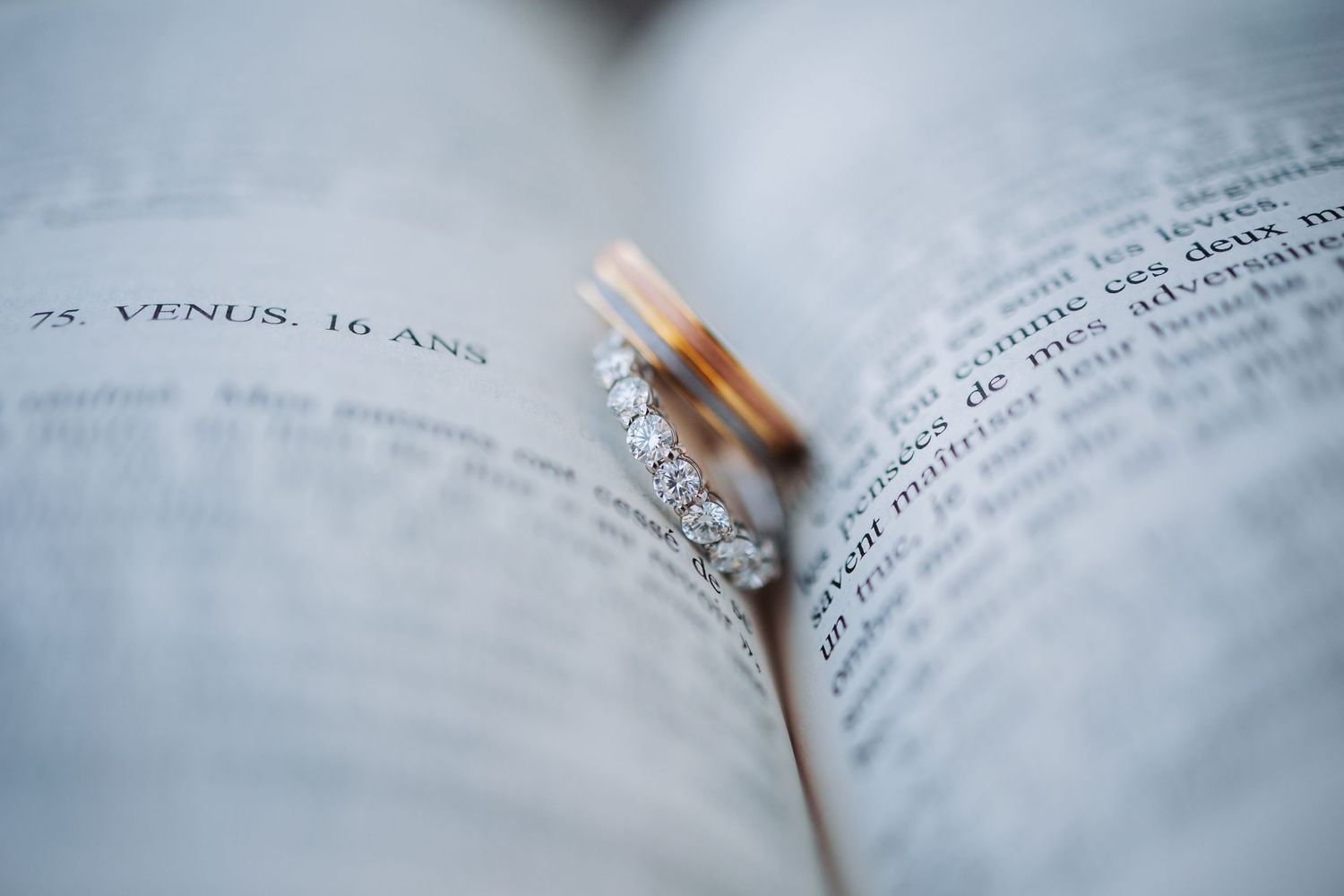 Wedding rings rest on open book pages with shallow depth of field.