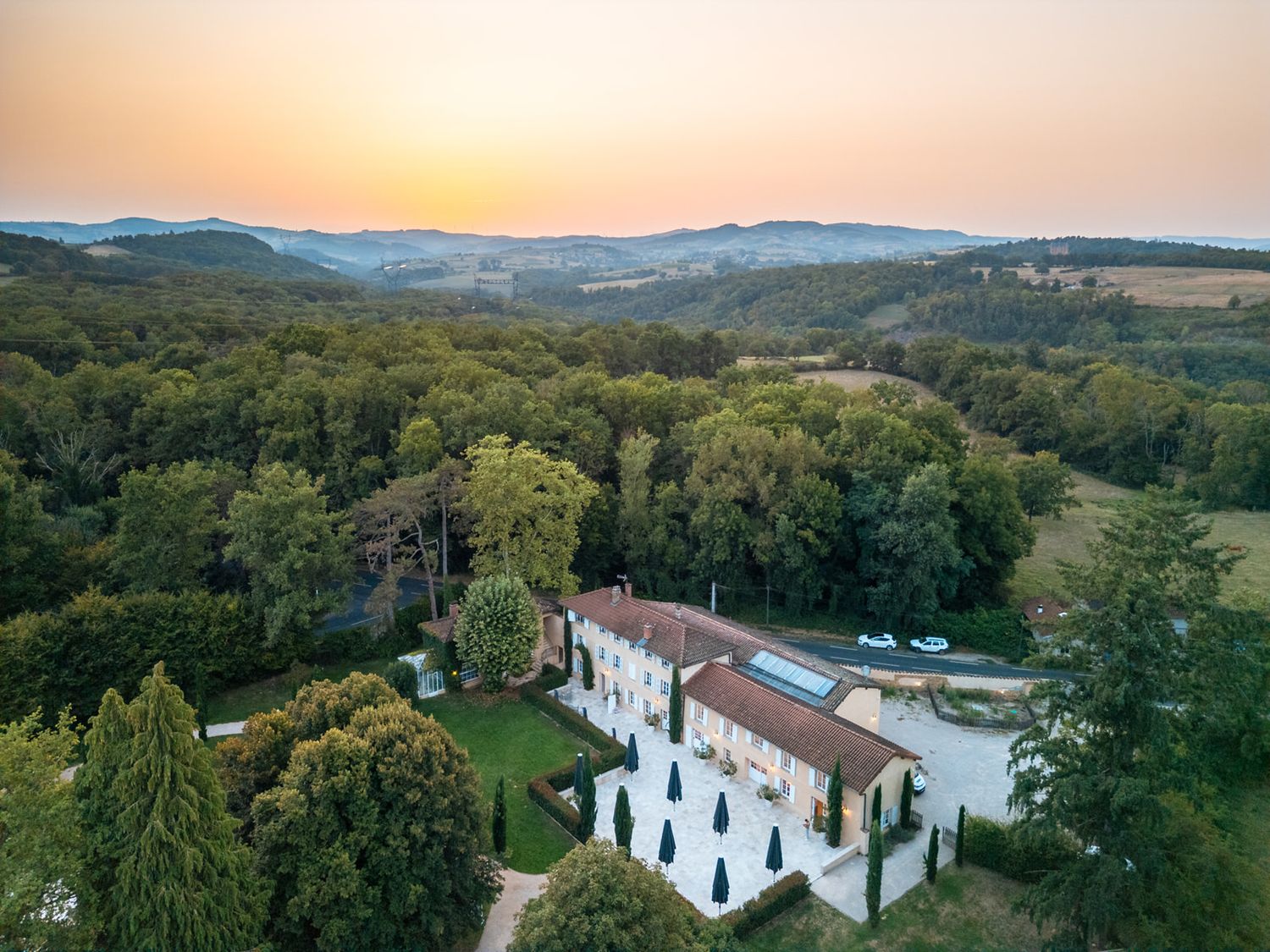 Aerial panoramic view of a white Mediterranean villa nestled in rolling green hills during golden sunset.