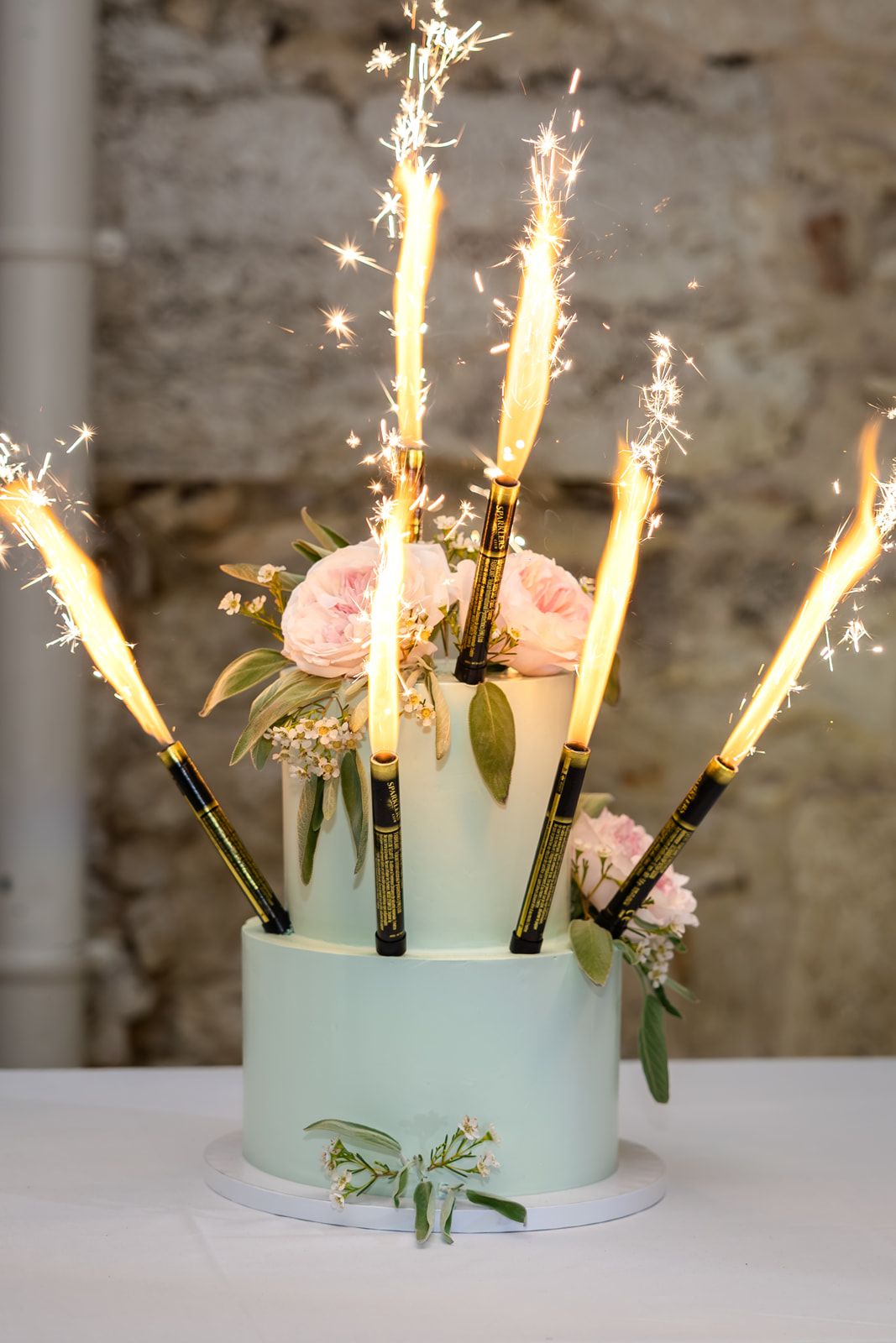 A mint green wedding cake decorated with pink roses and sparkler candles creating a magical display of light.