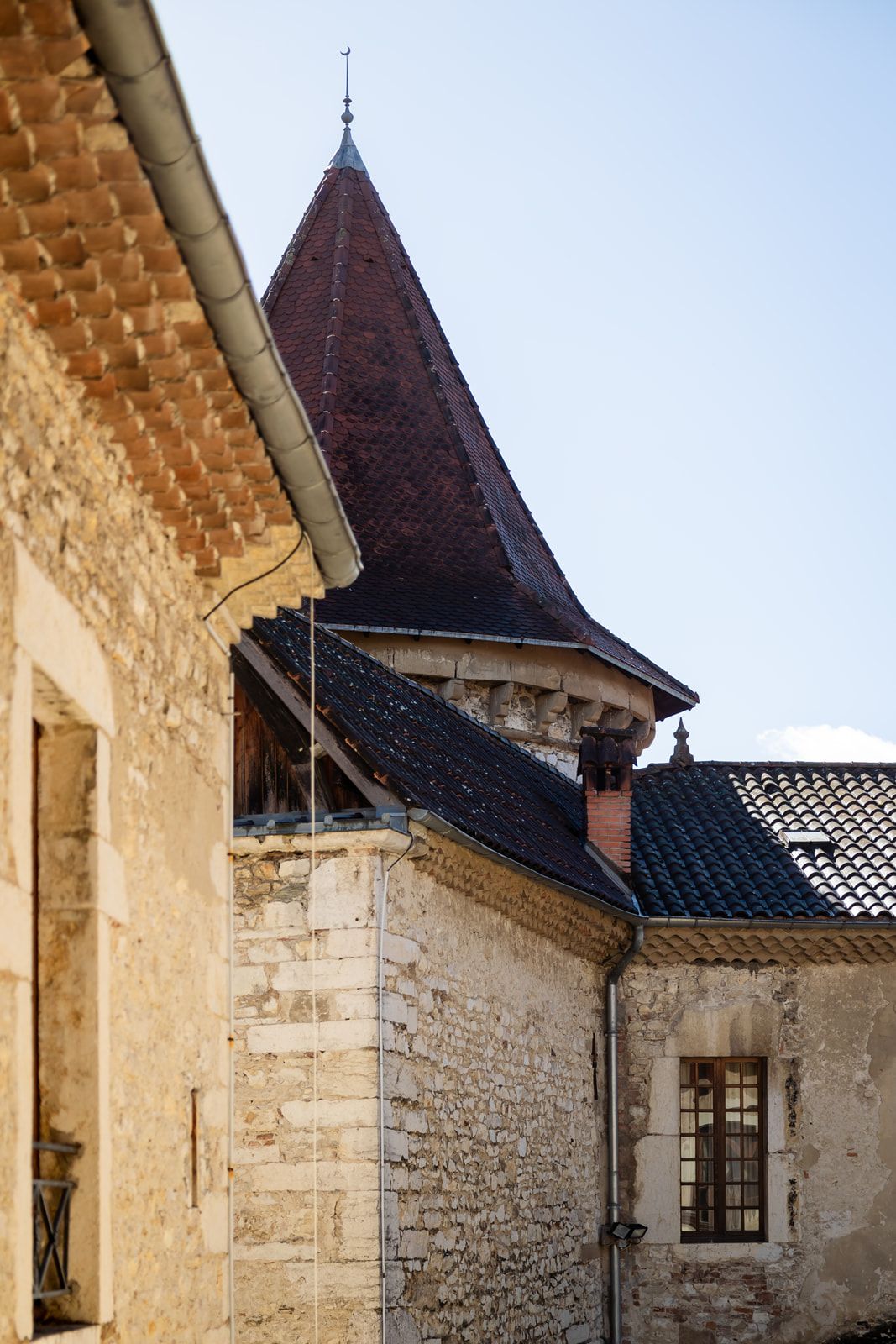 Medieval stone building with steep dark spire tower and window against light stone walls and tiled roof.