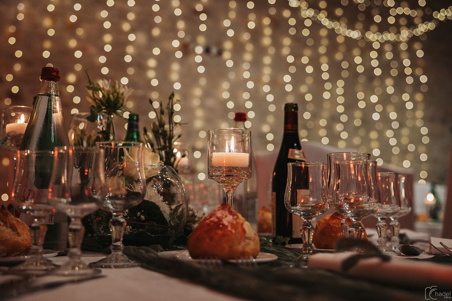 A romantic candlelit dinner table setting with twinkling string lights and wine glasses creating an intimate atmosphere.
