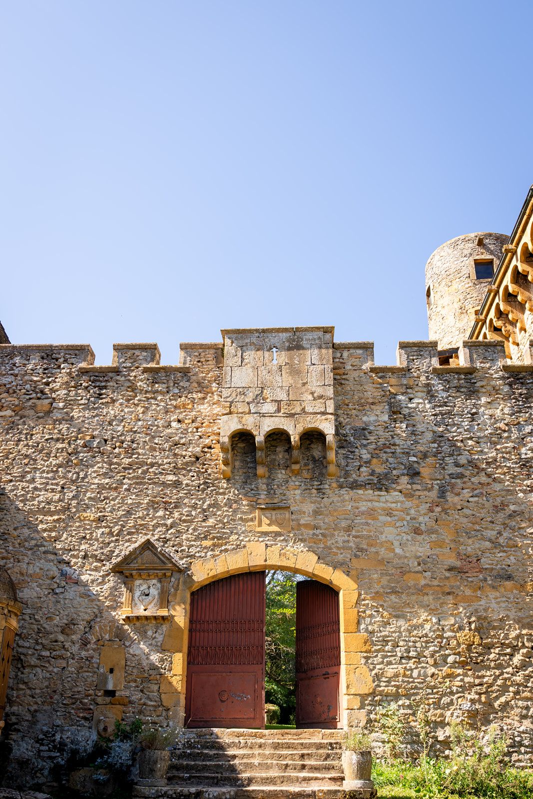Ancient stone fortress wall with arched doorways and stone staircase leading to battlements in warm sunlight.