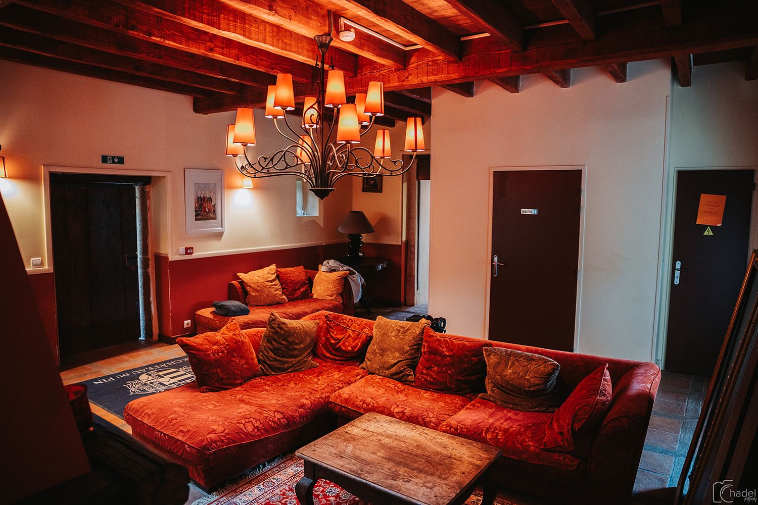Luxury hotel room with red bedding, dark wood beams, and elegant chandelier lighting creates a romantic ambiance.