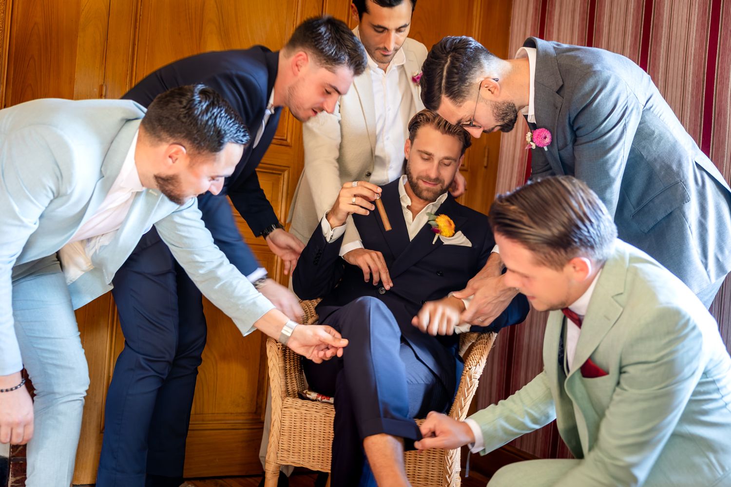A group of groomsmen in formal attire help each other get ready before a wedding ceremony.
