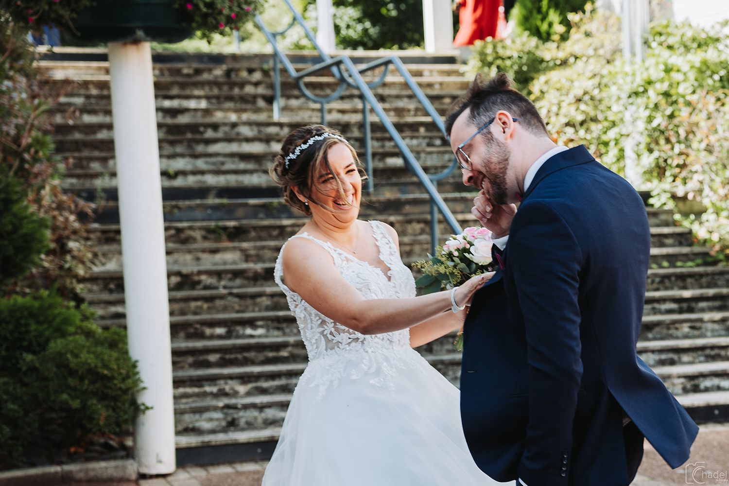 A couple shares a romantic moment during their wedding ceremony under white pillars in an outdoor garden setting.