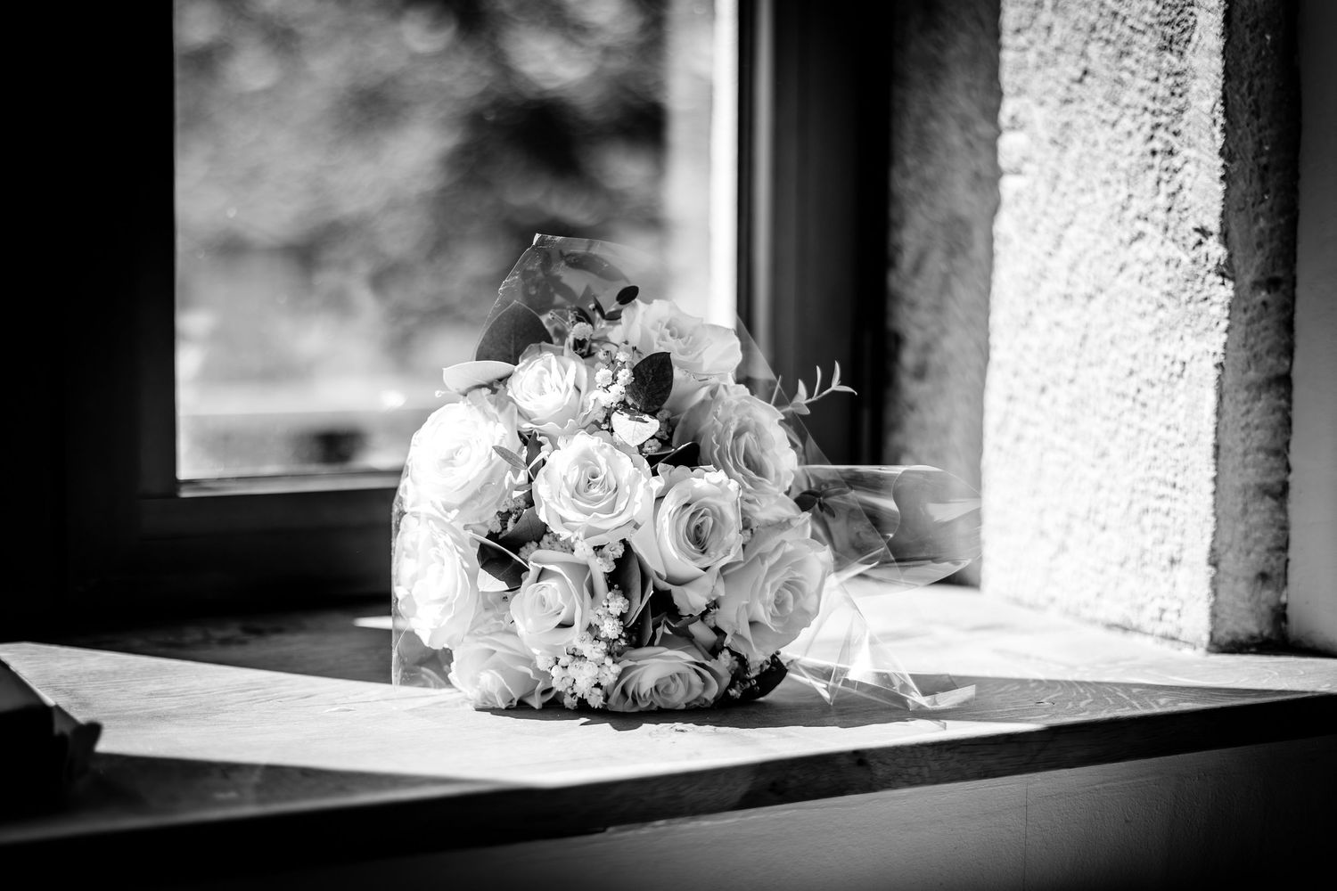 Black and white wedding detail shot with floral bouquet on a windowsill.