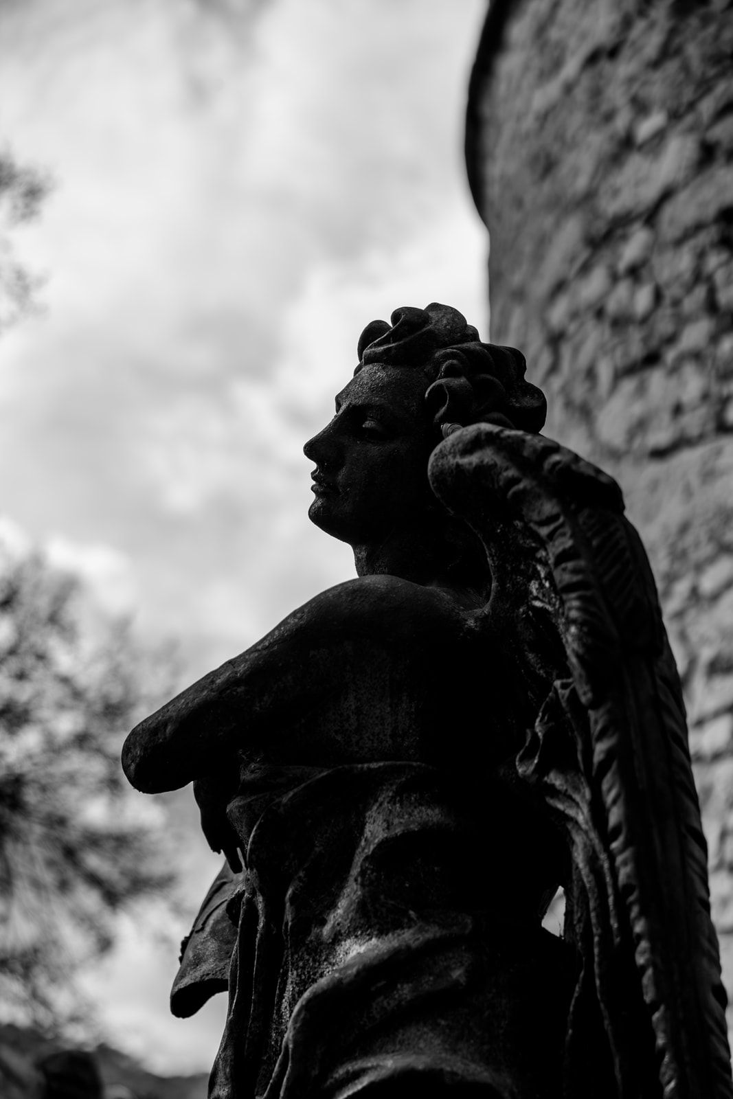 Black and white low angle view of a classical stone statue silhouetted against a cloudy sky.