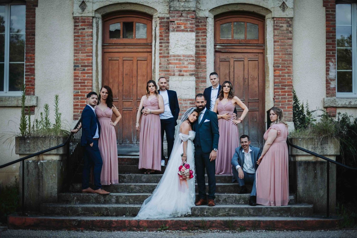 Wedding party poses together in front of historic brick building with arched doorways.