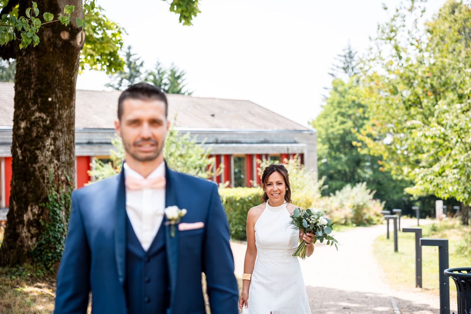 A wedding party poses outdoors in navy blue attire under green trees on a sunny day.