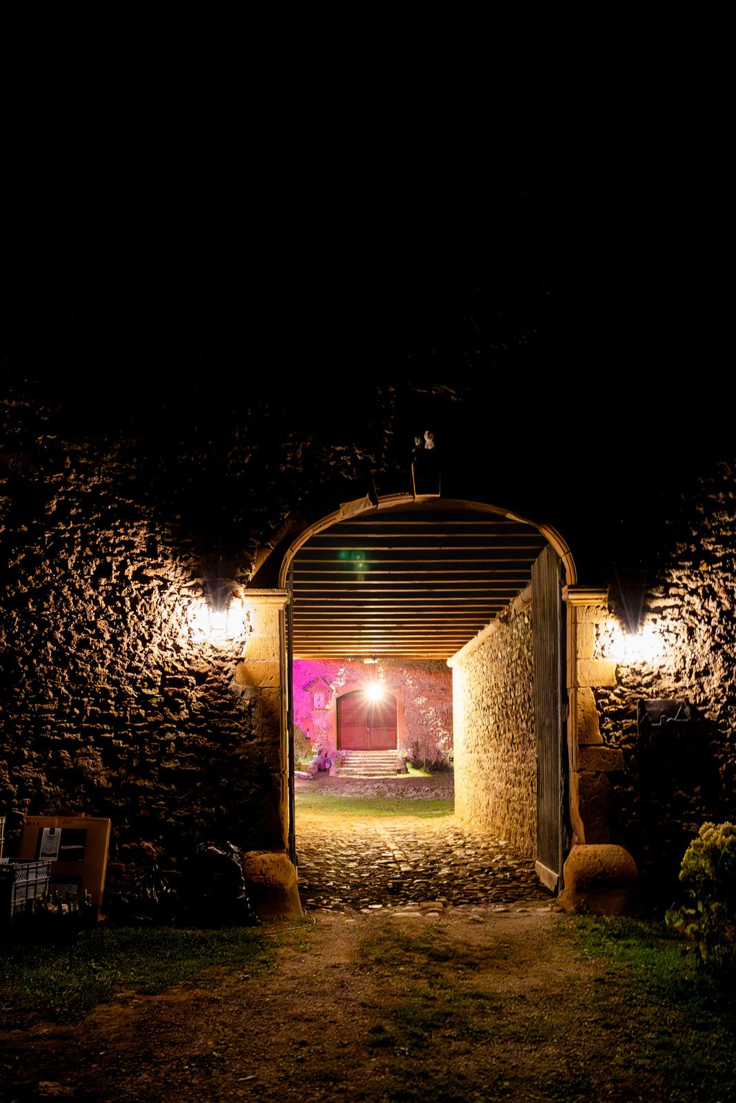 Stone archway illuminated by warm lights at night creates a dramatic entrance to a rustic garden path.