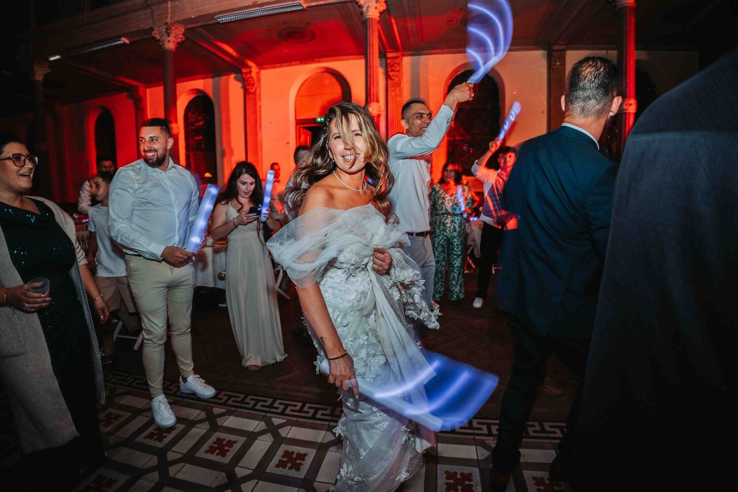 Wedding party dancing under moody red lighting in an elegant venue.