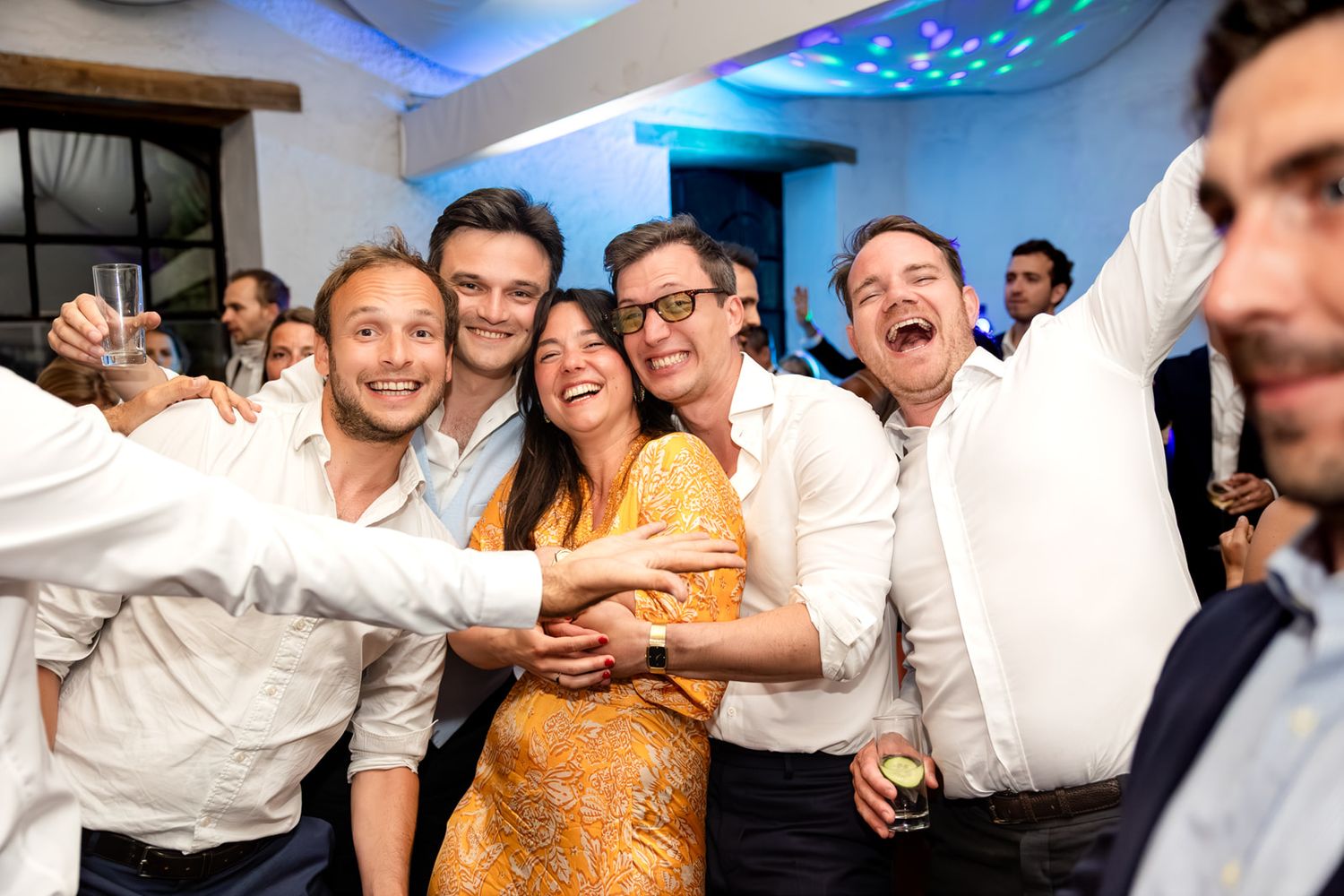 Group of friends celebrating at a wedding reception, taking a selfie and laughing together on the dance floor.