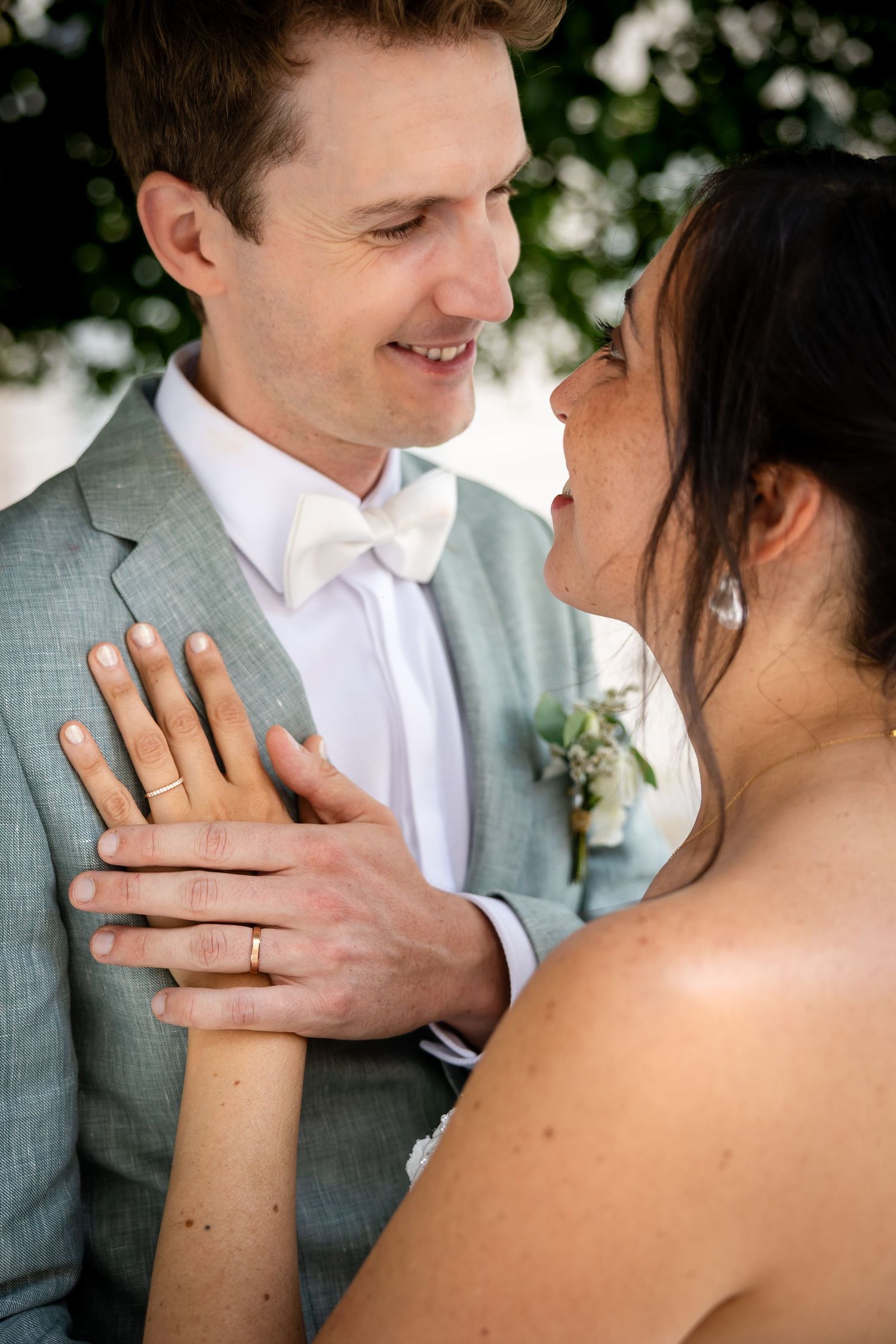 Close-up wedding portrait showing hands and rings against light colored attire.