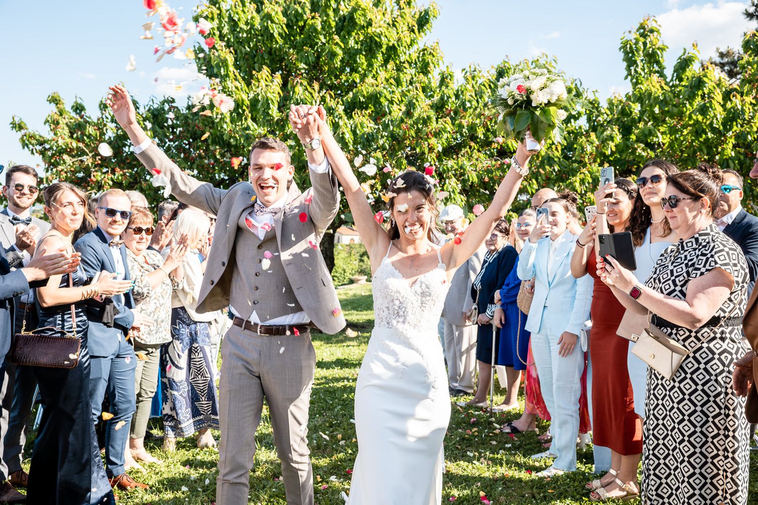 Wedding guests celebrate outdoors by throwing flower petals and confetti in a joyful group celebration.