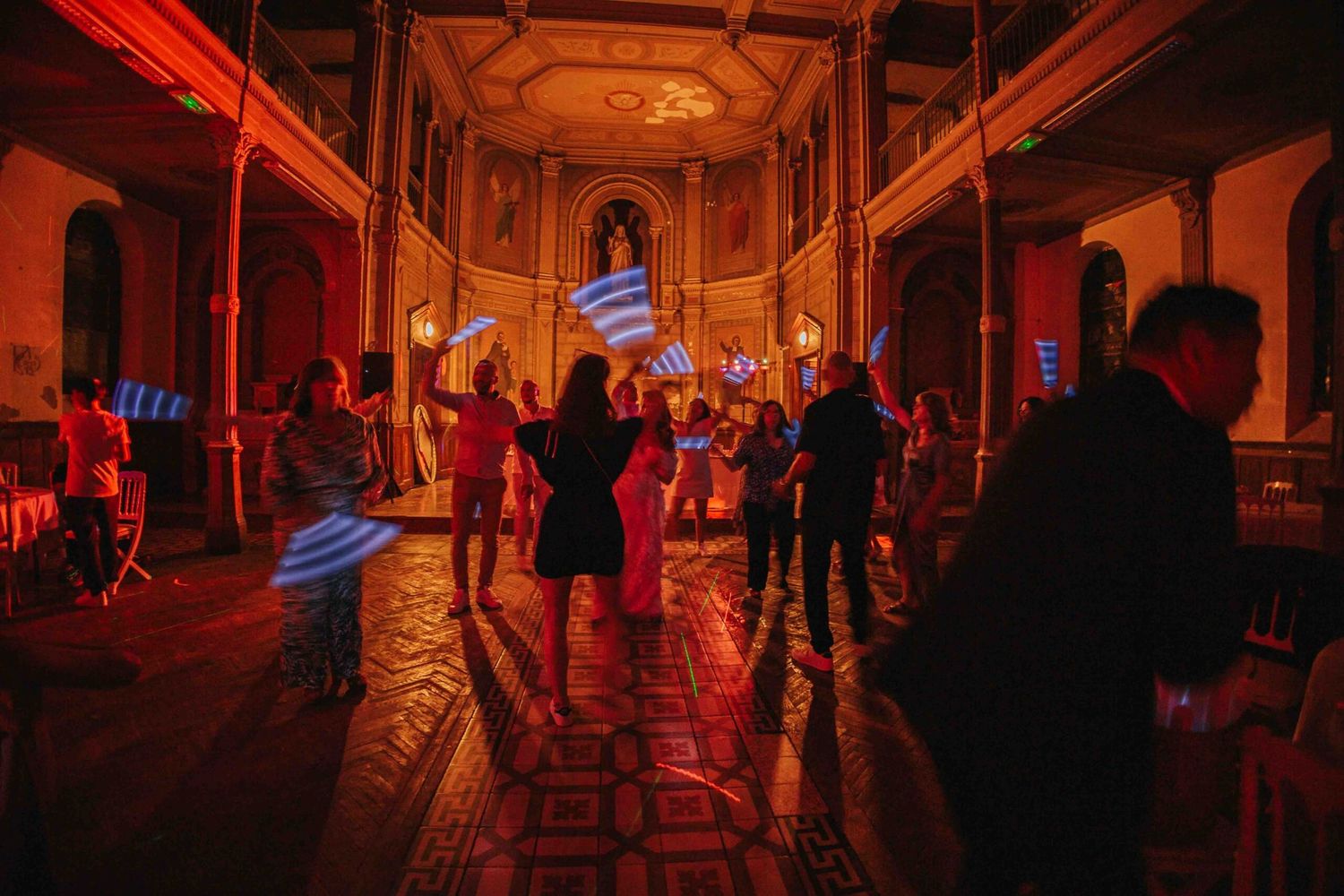 People dancing in a dimly lit room with red lighting and neon blue accents creating a moody nightclub atmosphere.