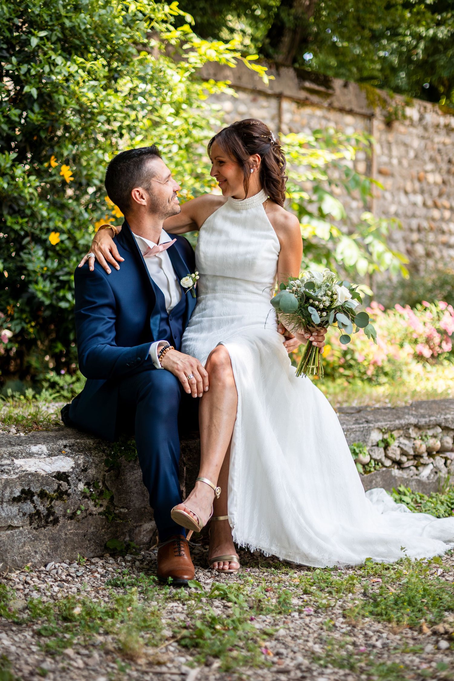Wedding couple shares romantic moments on rustic stone path surrounded by greenery.