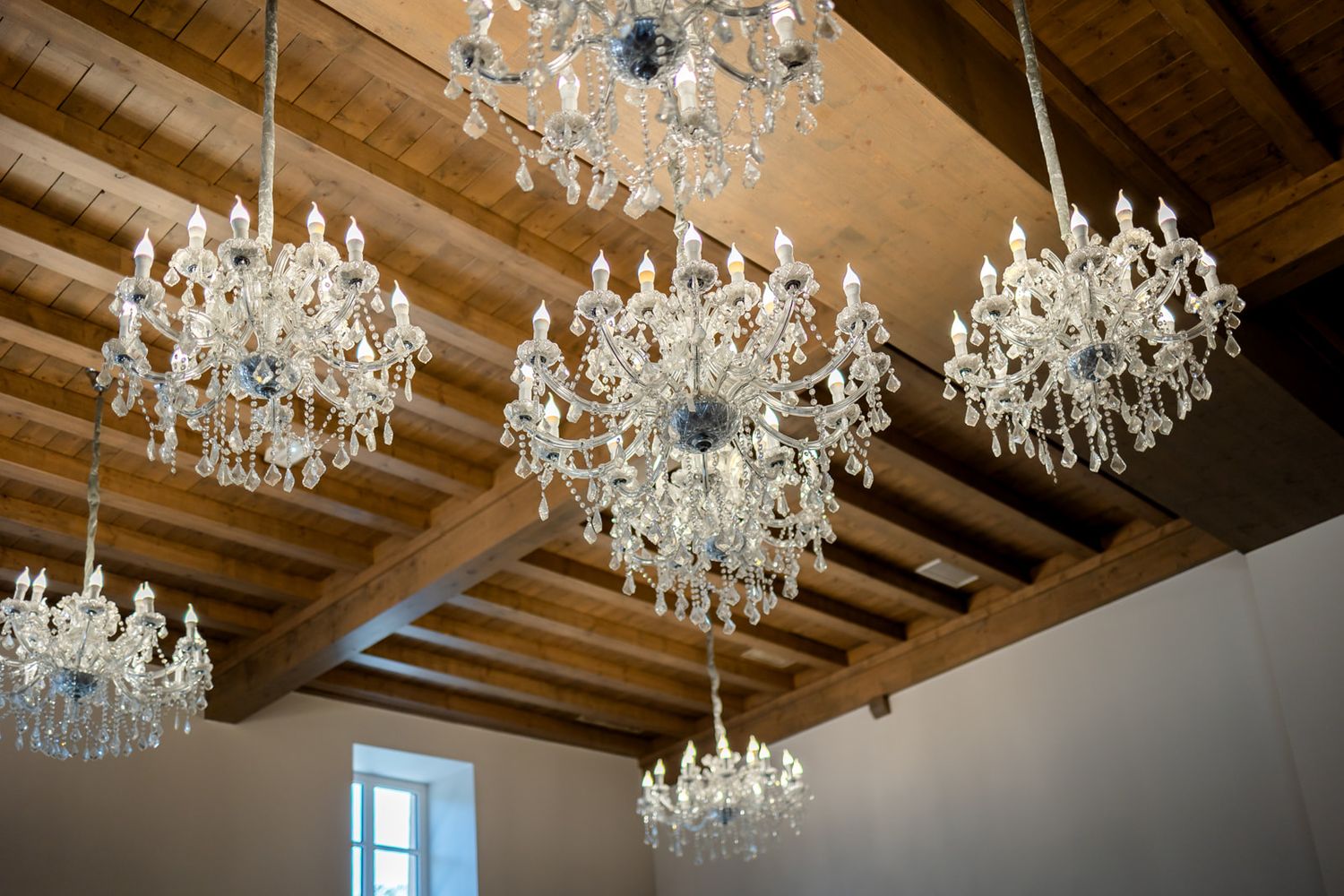 Multiple ornate crystal chandeliers hang from a wooden beam ceiling in an elegant interior space.