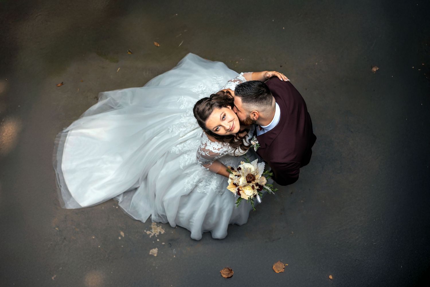 Dramatic aerial view of newlyweds on dark floor with bride's white dress creating elegant contrast.