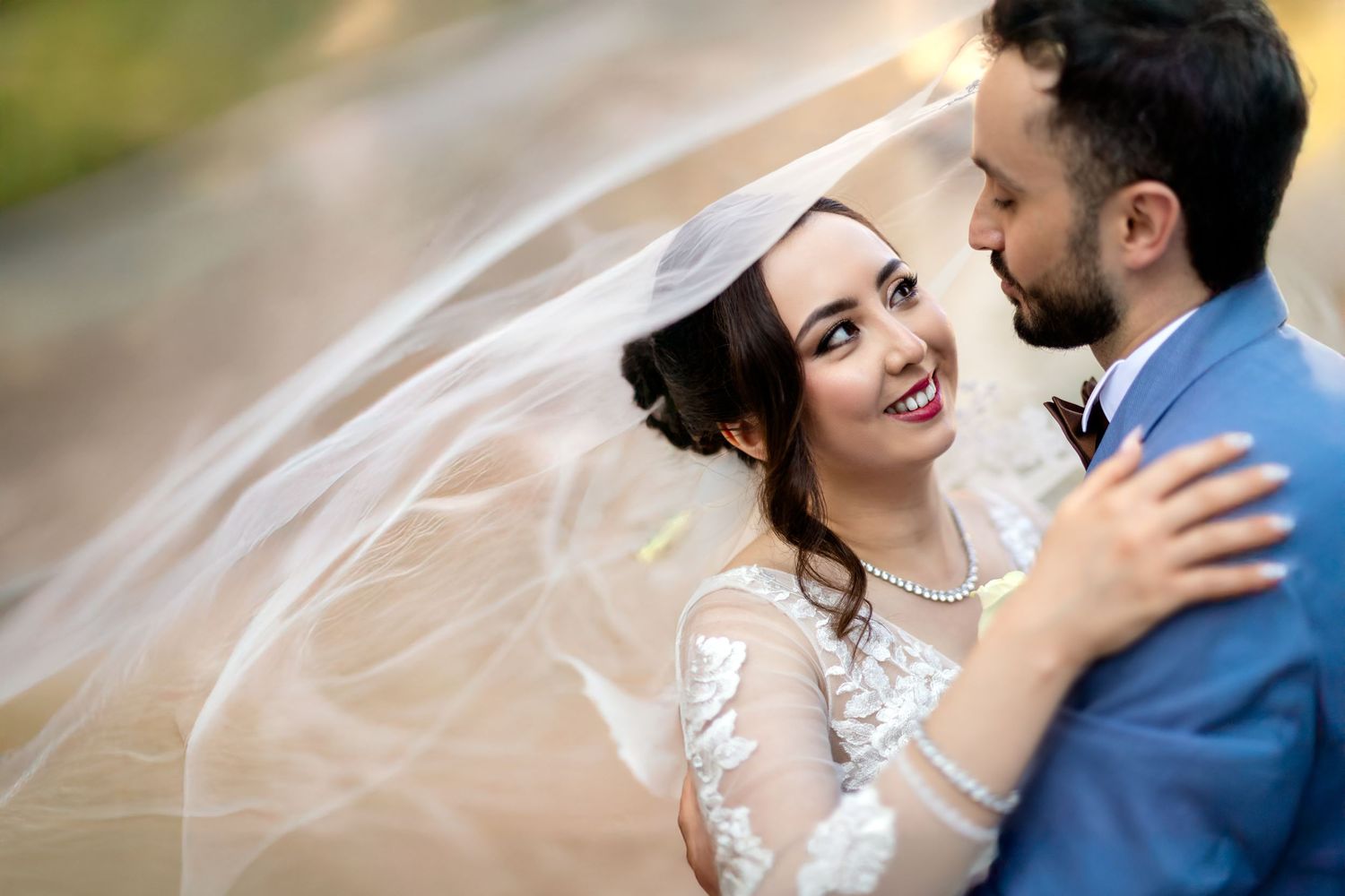 A romantic wedding couple embraces in an outdoor setting with soft lighting and flowing veil.