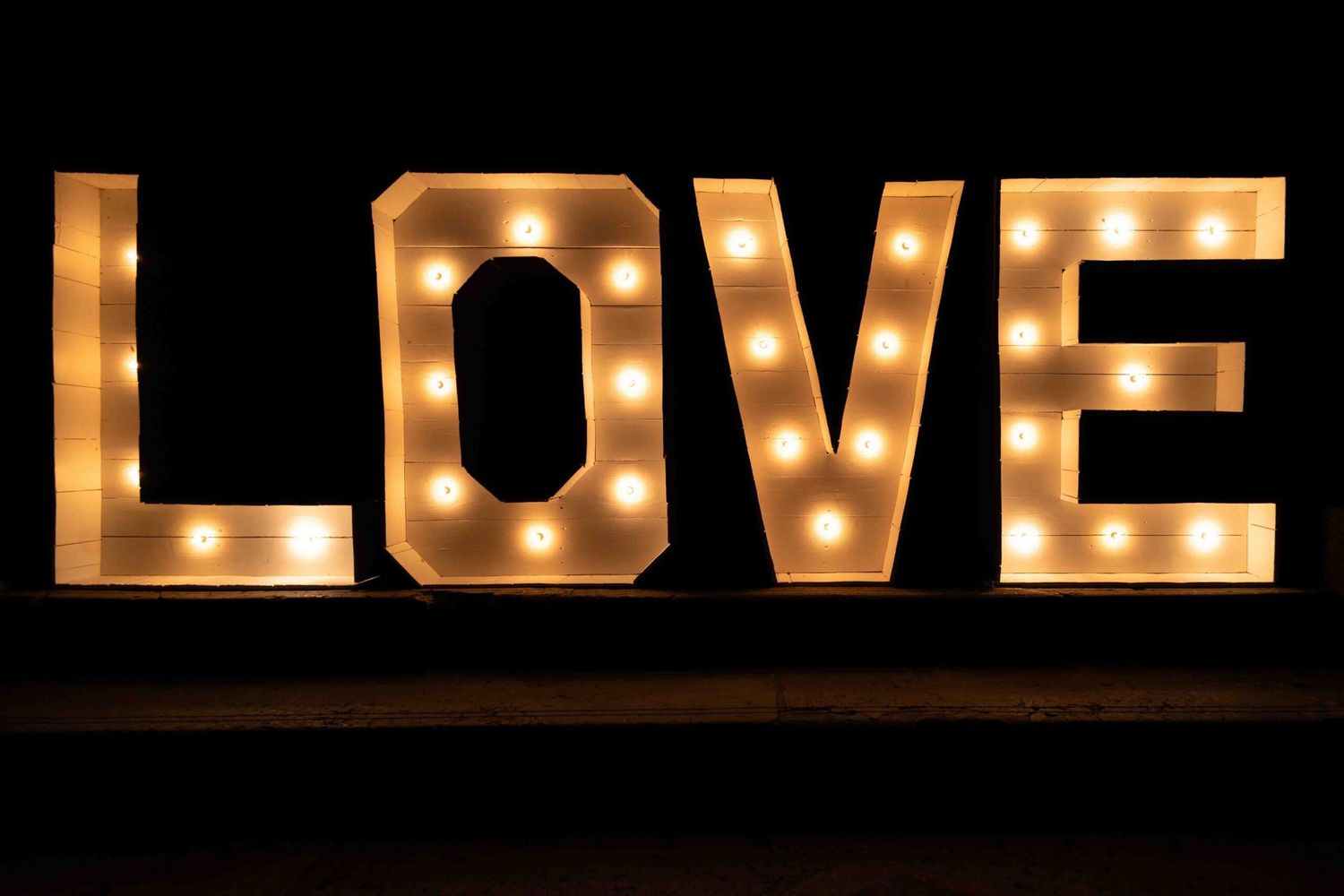Illuminated letters spelling LOVE with glowing marquee bulbs against a dark background.