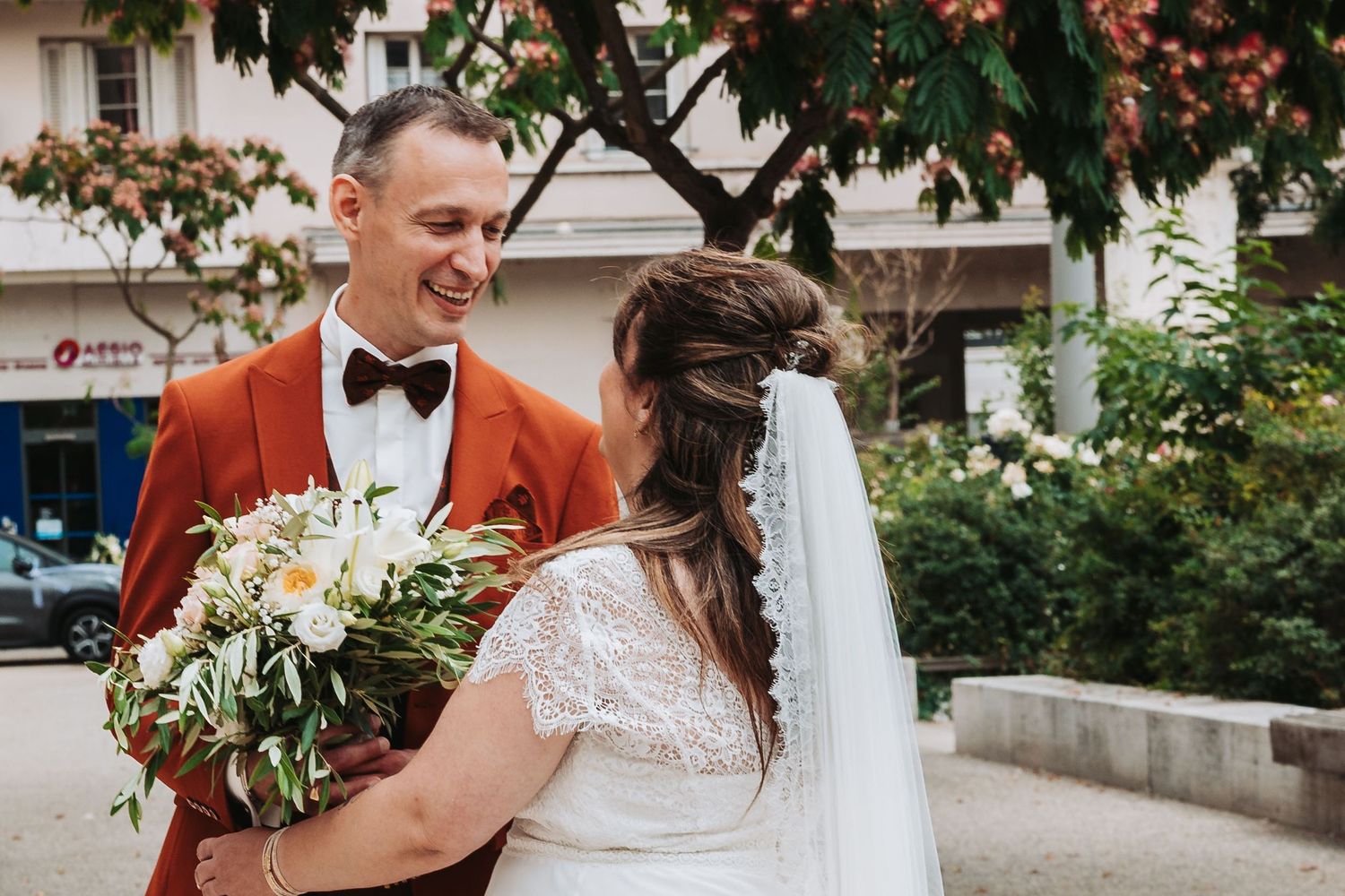 A happy wedding couple shares a candid moment outdoors surrounded by greenery and flowers.
