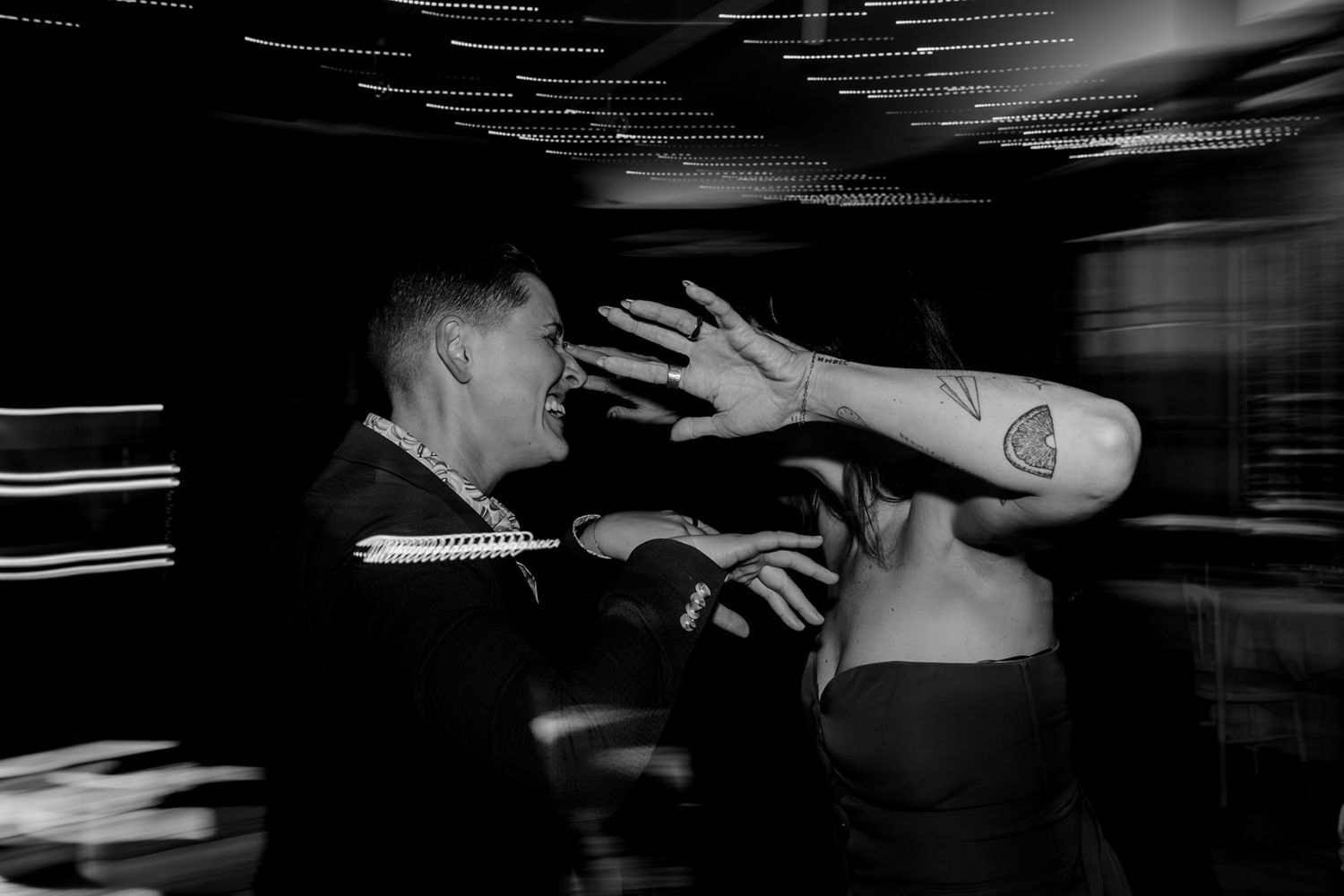 Black and white motion blur photo shows a person dancing with outstretched arms in a dark setting.