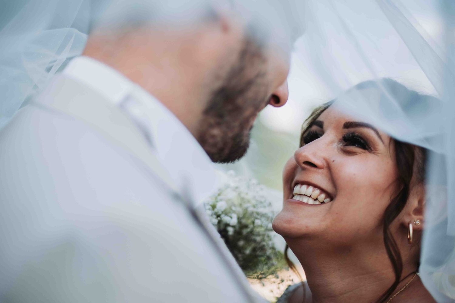 Close-up wedding portrait under a flowing veil with joyful expressions.