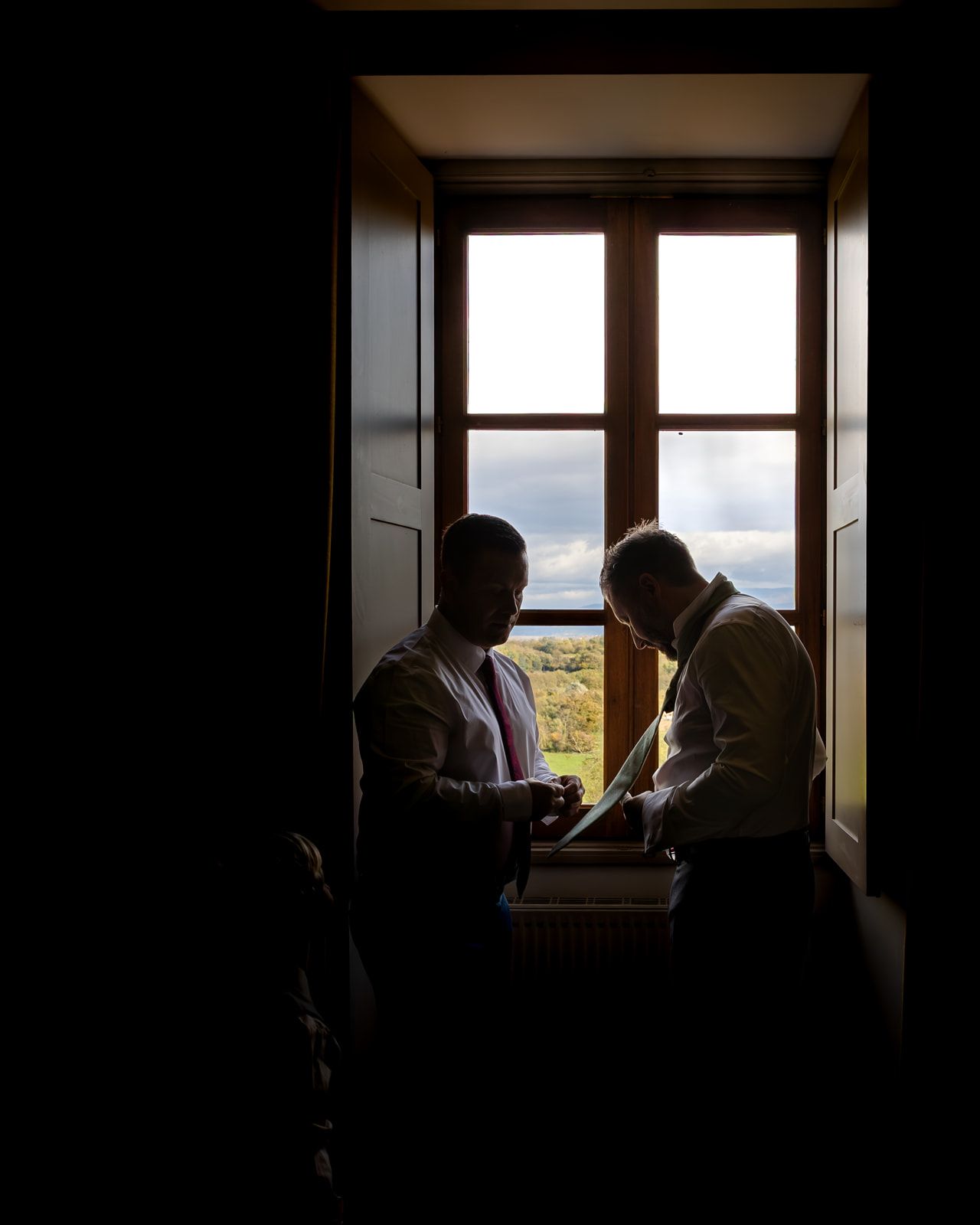 Silhouetted figures stand by a window, creating a dramatic contrast against the bright natural light streaming in.