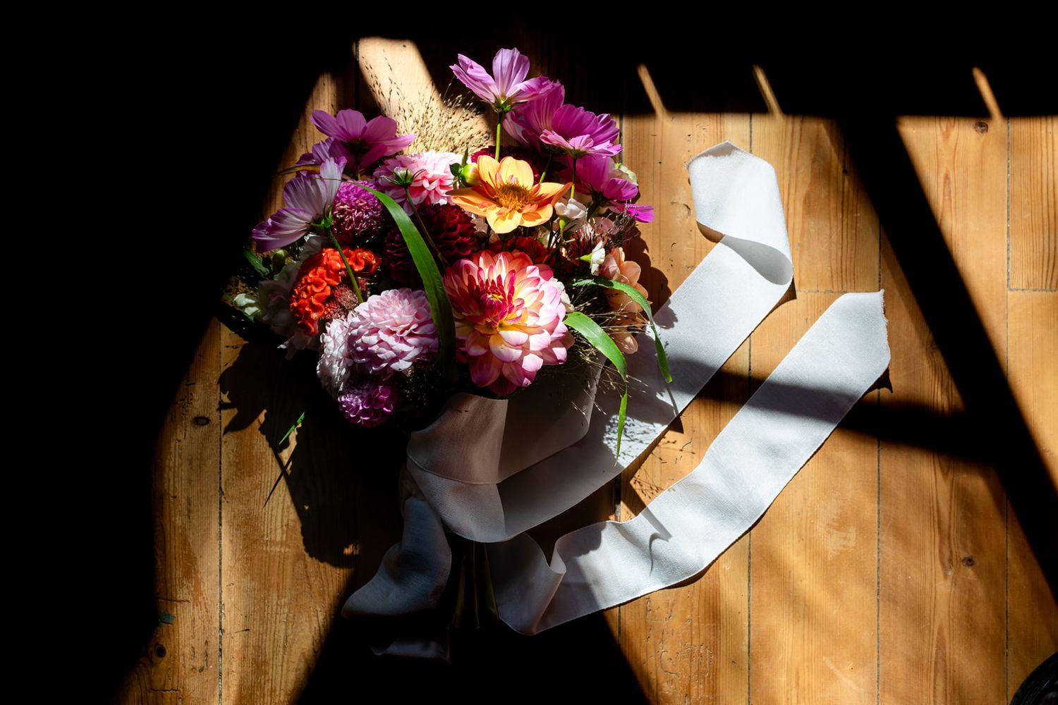 Vibrant pink and purple flower bouquet casting dramatic shadows on rustic wooden surface in natural sunlight.