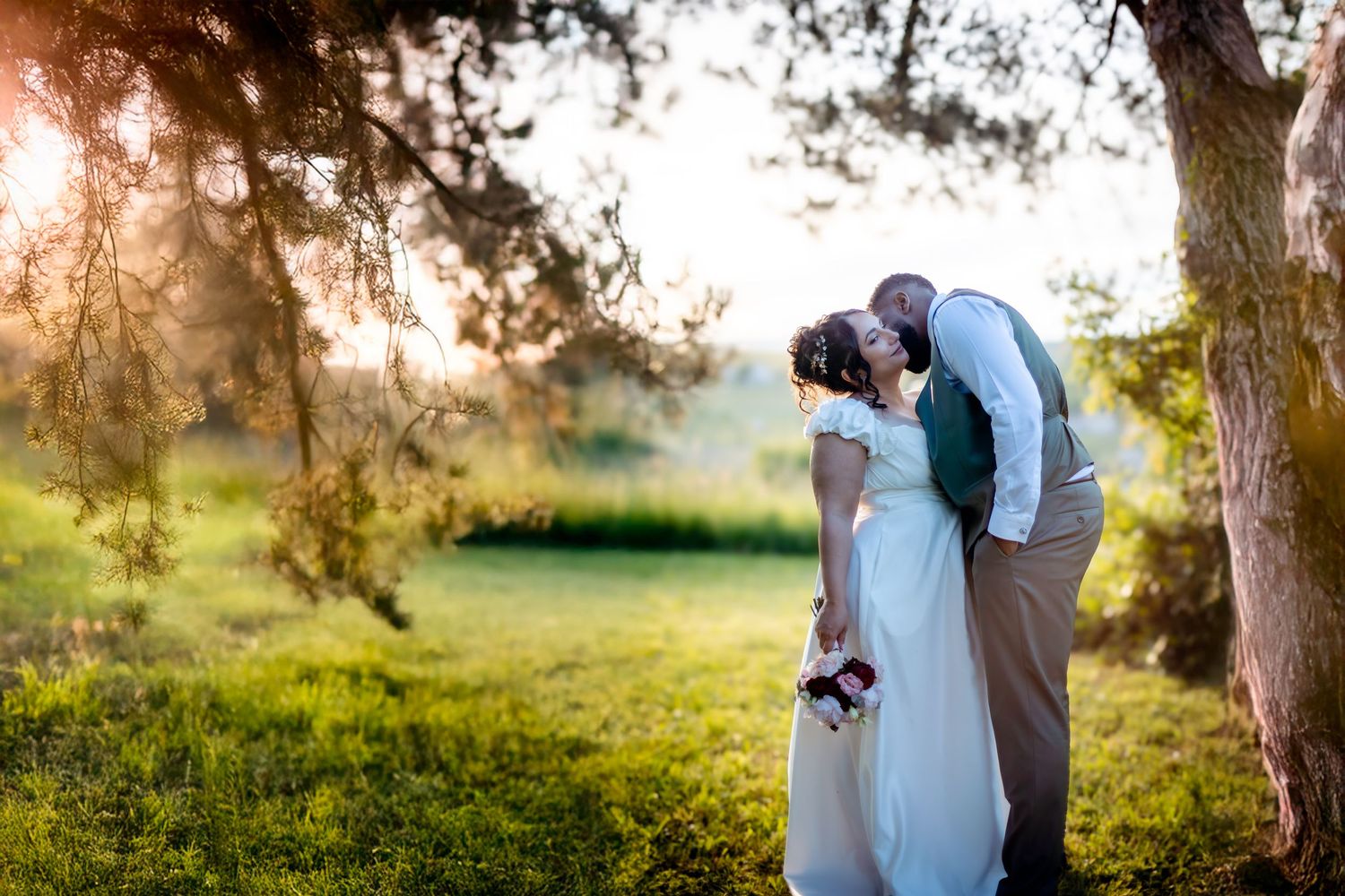 Romantic wedding couple embraces in a sunlit garden setting with golden hour lighting.