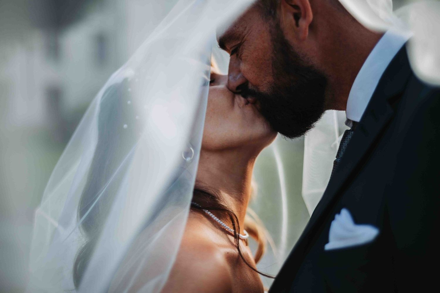 Tender close-up moment between newlyweds with flowing white veil in natural light.