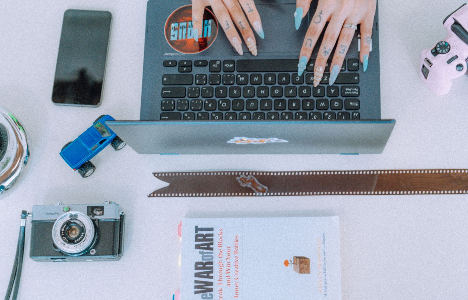 Hands typing on laptop keyboards in a clean white workspace with office supplies and electronics.