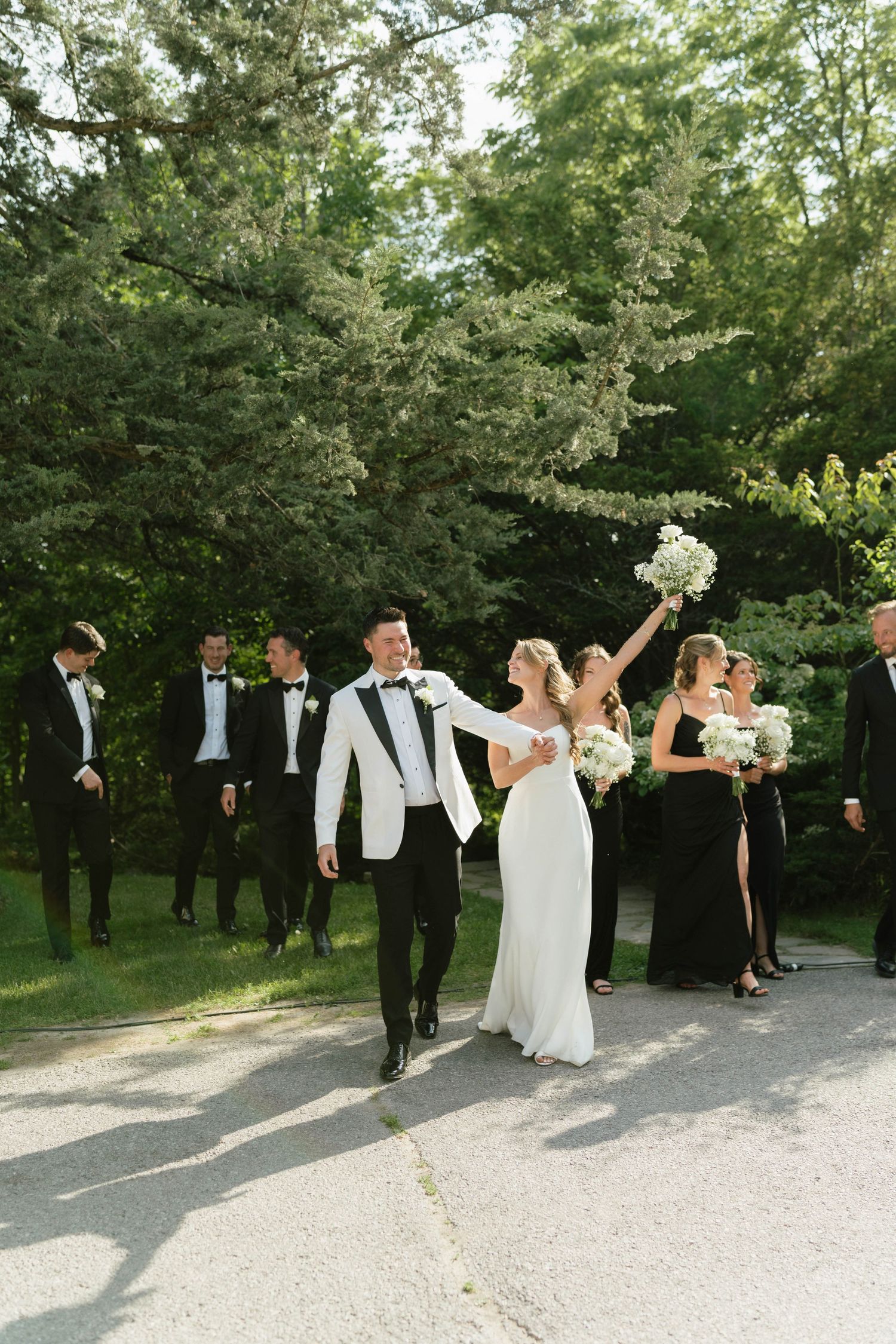 Wedding party walks along a garden path with bridal couple leading the celebration.