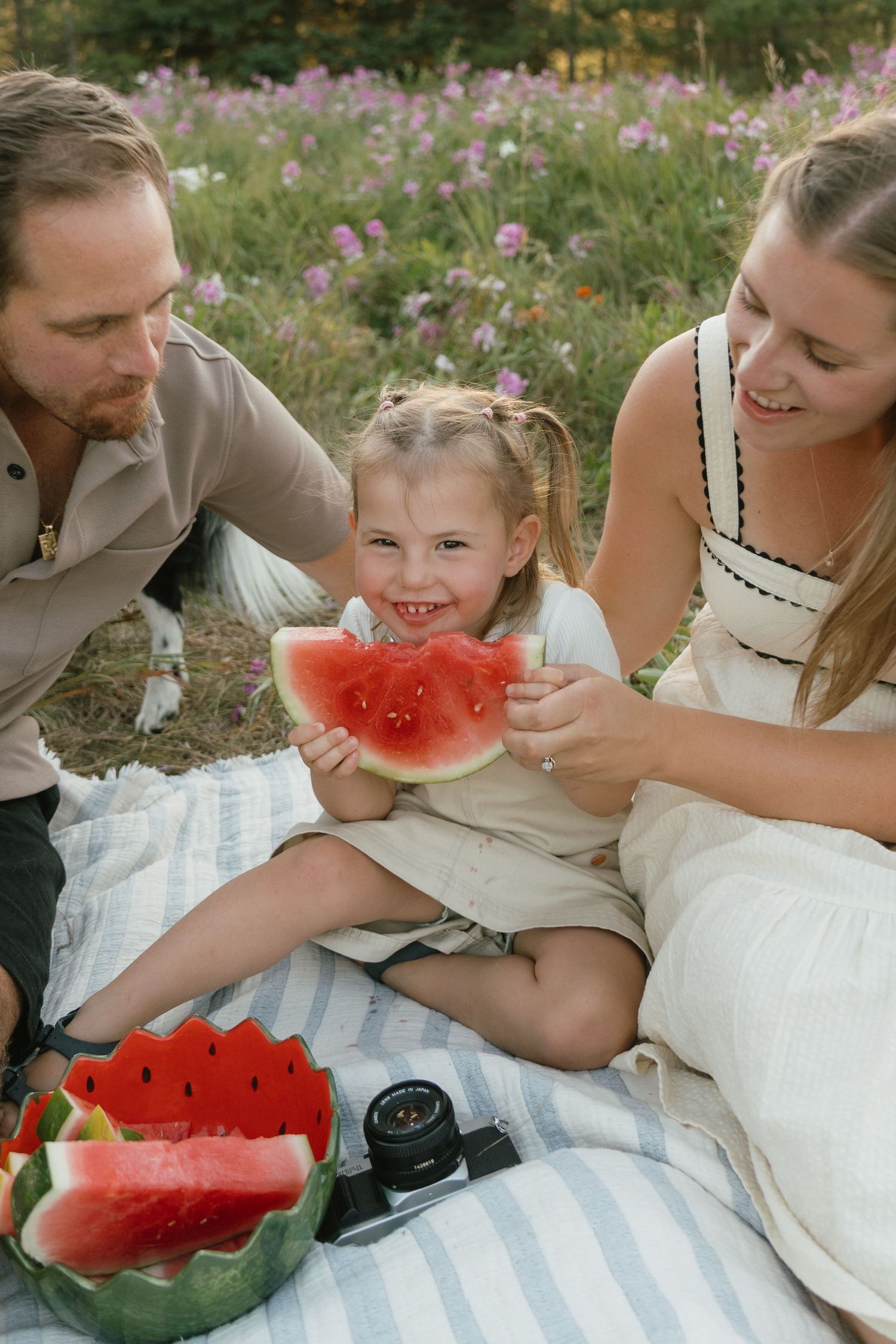 Family enjoying watermelon slices during a summer picnic on a blanket surrounded by wildflowers.
