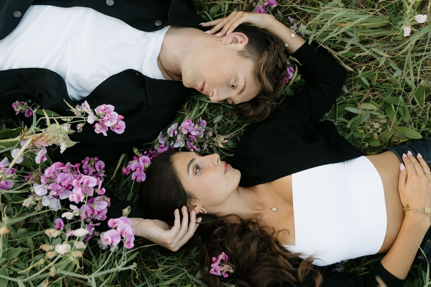 A romantic couple lying in a field of pink wildflowers during a dreamy outdoor photoshoot.