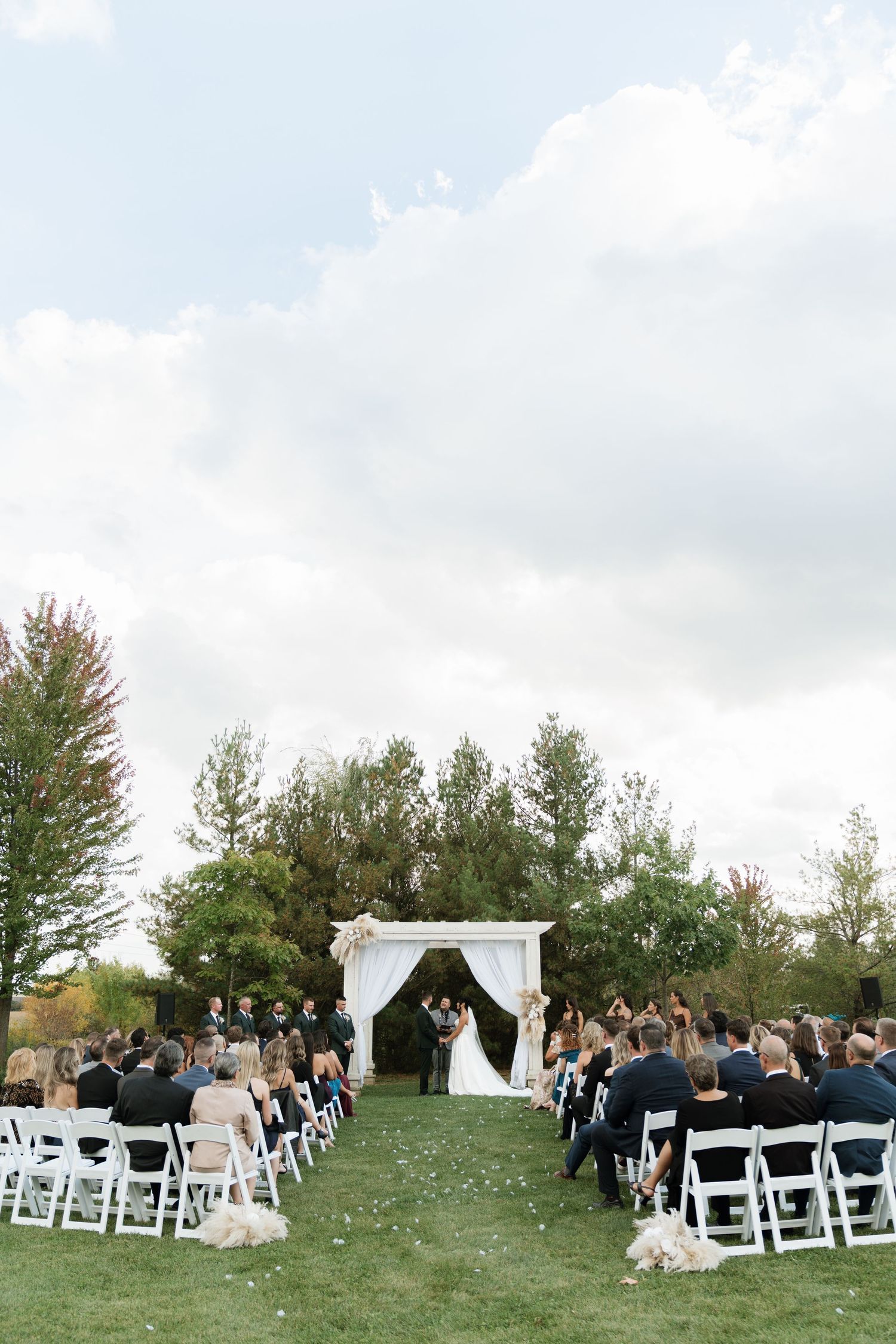 Outdoor wedding ceremony setup with white chairs and arch on grassy hillside.
