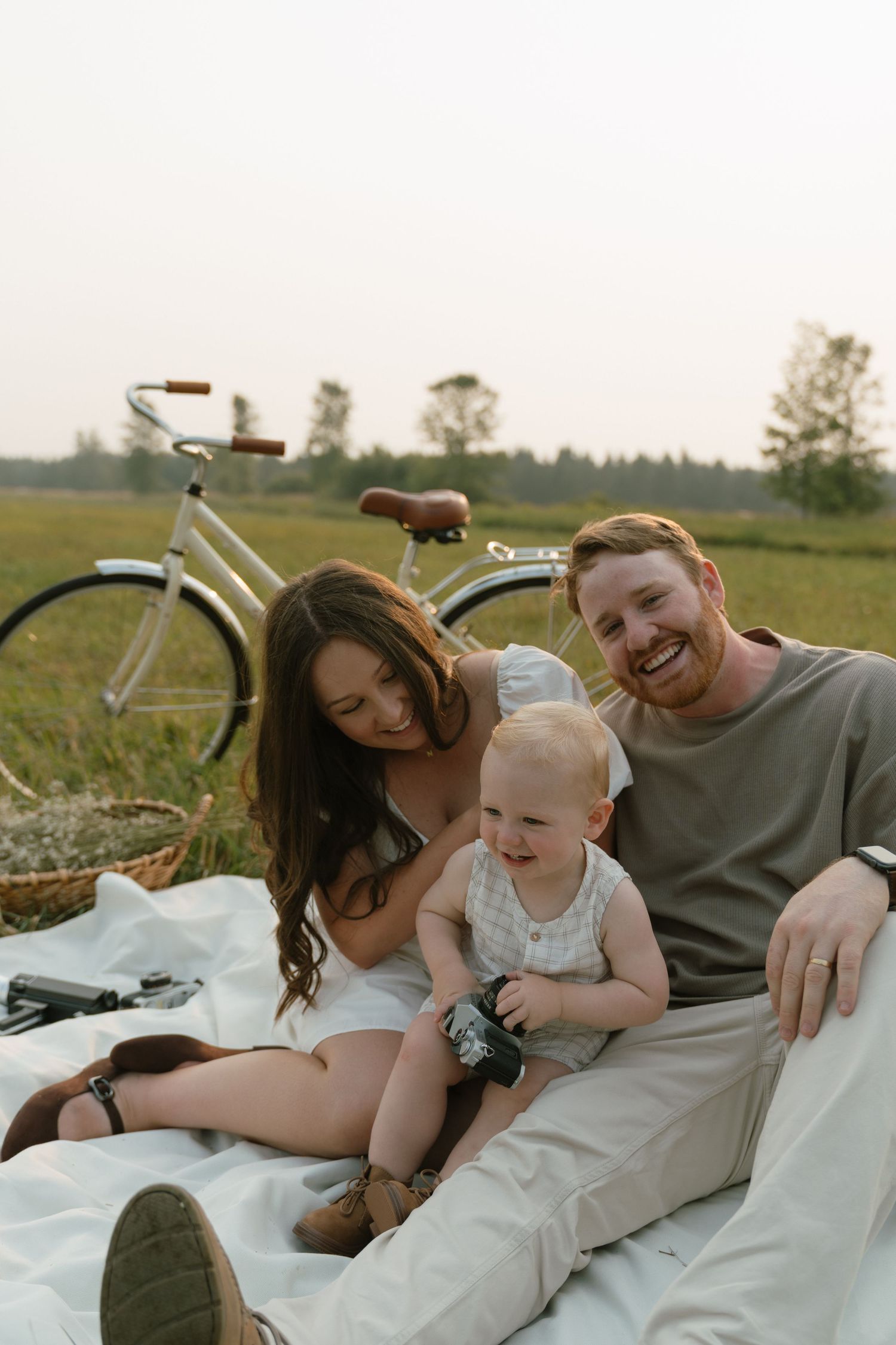 Family relaxing on white blanket in grassy field with vintage bicycle.