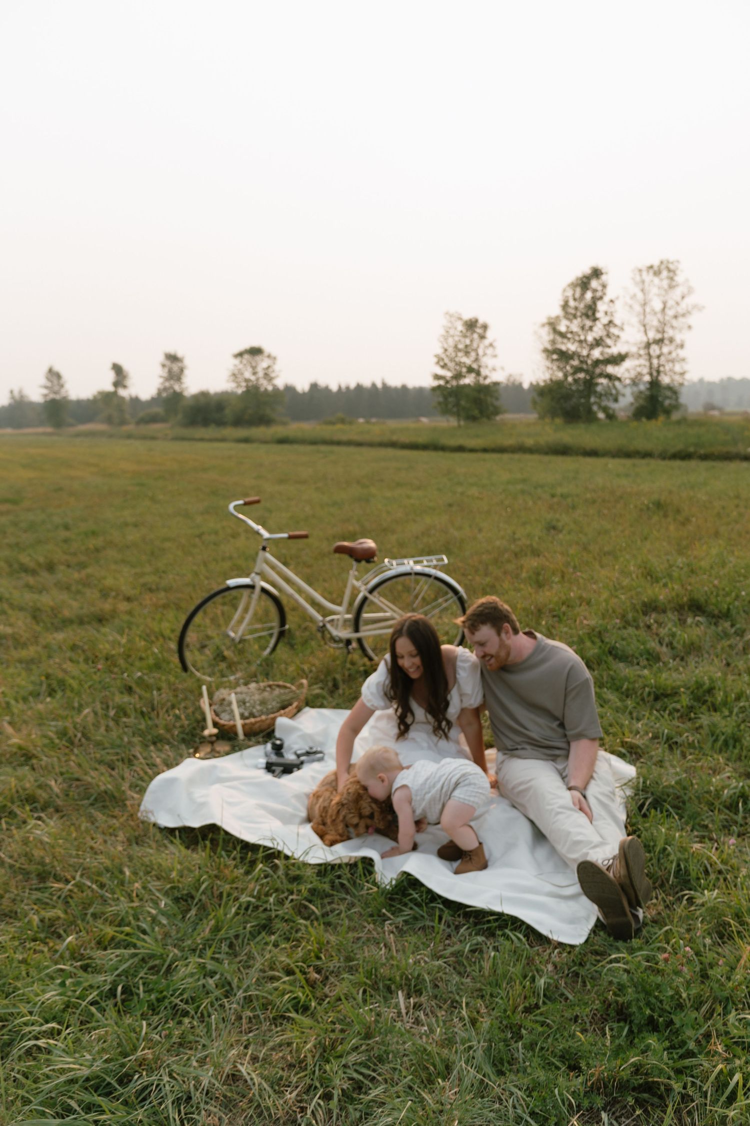 Family lying on blanket in meadow with vintage bicycle at golden hour.
