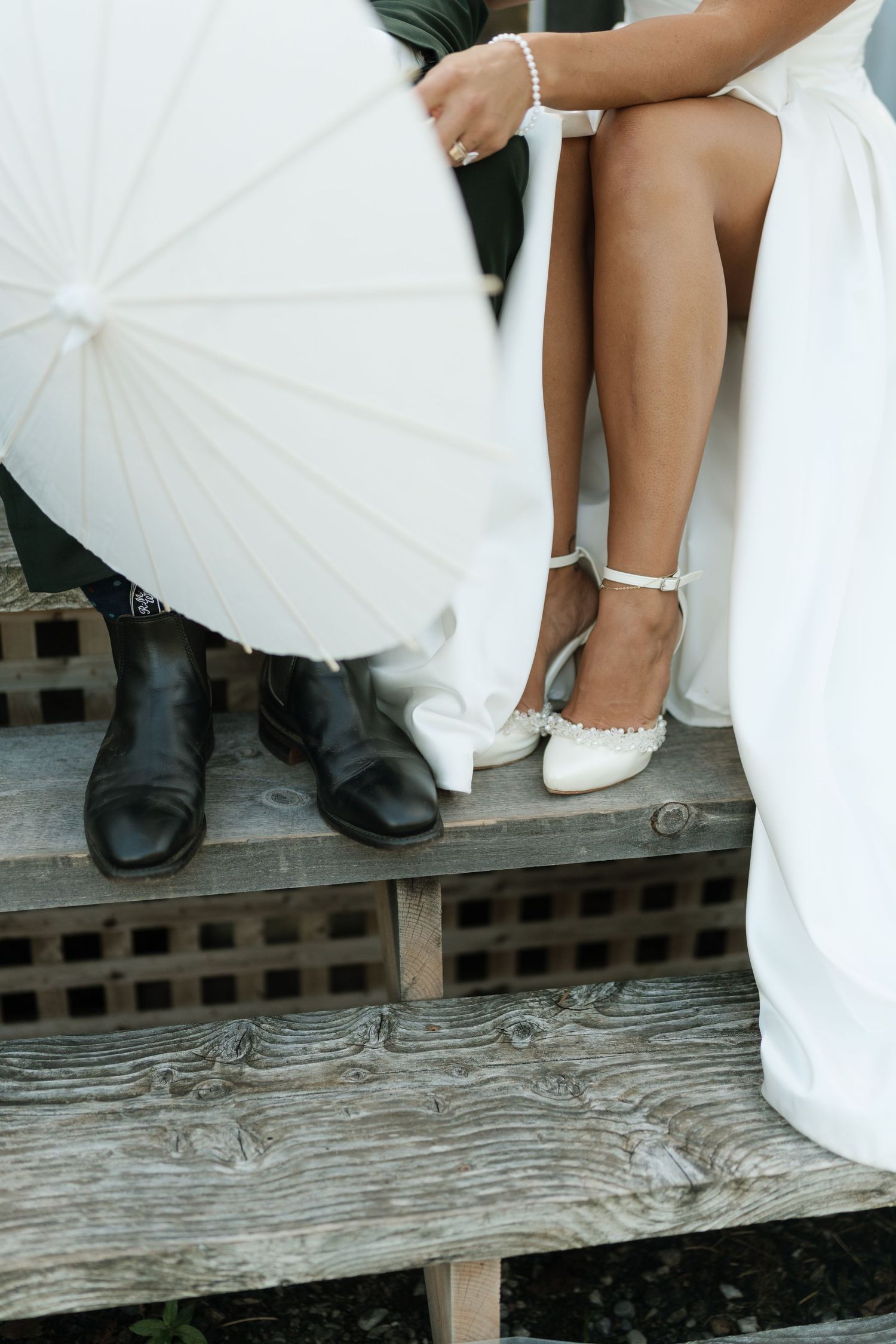 Close-up of wedding shoes and white parasols on rustic wooden deck.