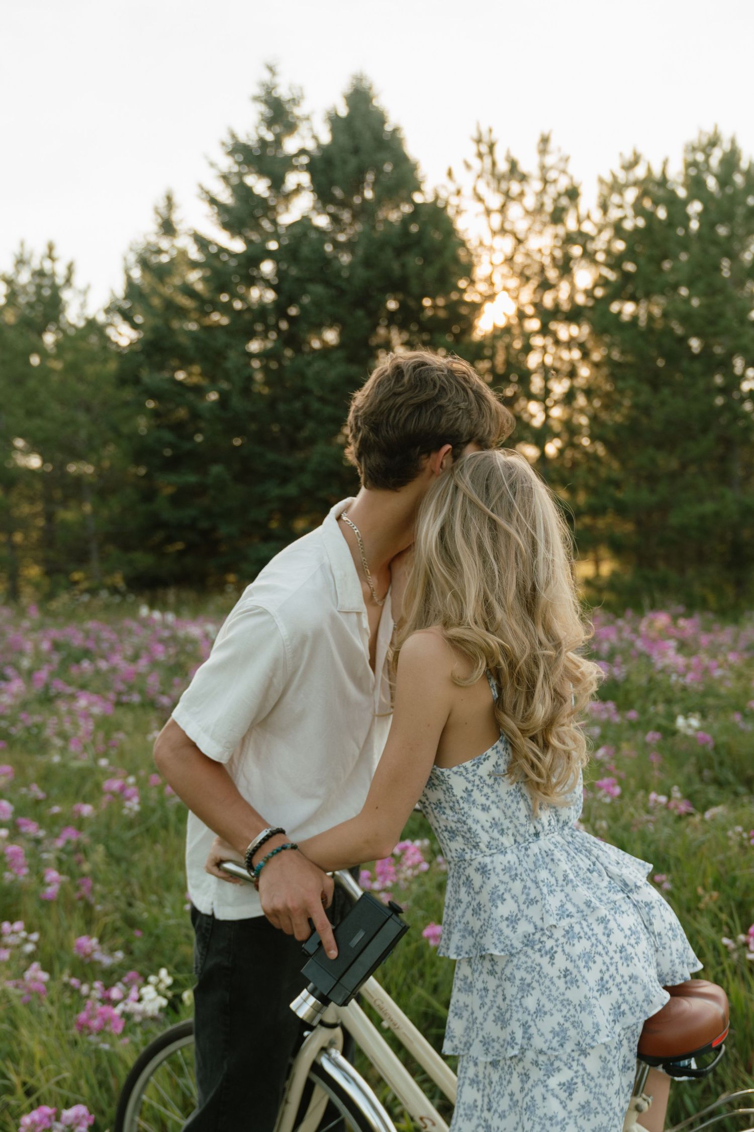 A romantic couple with a vintage bicycle in a blooming flower field at sunset.